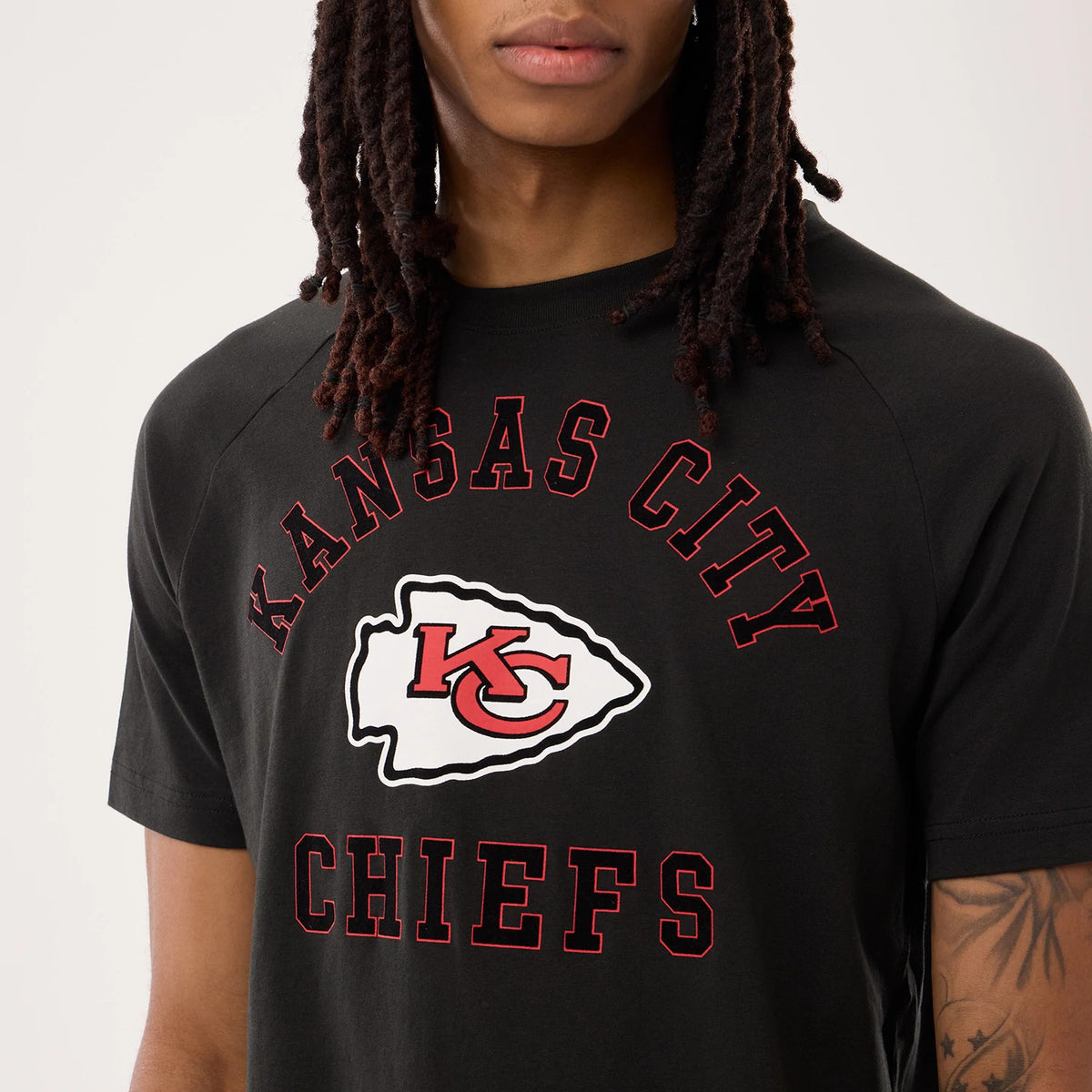 New Era Kansas City Chiefs NFL Sideline 2026 Black T-Shirt, front view on a model showing red 'Kansas City Chiefs' lettering and a large white arrowhead with a red KC logo, styled simply with tattoos on the arm.