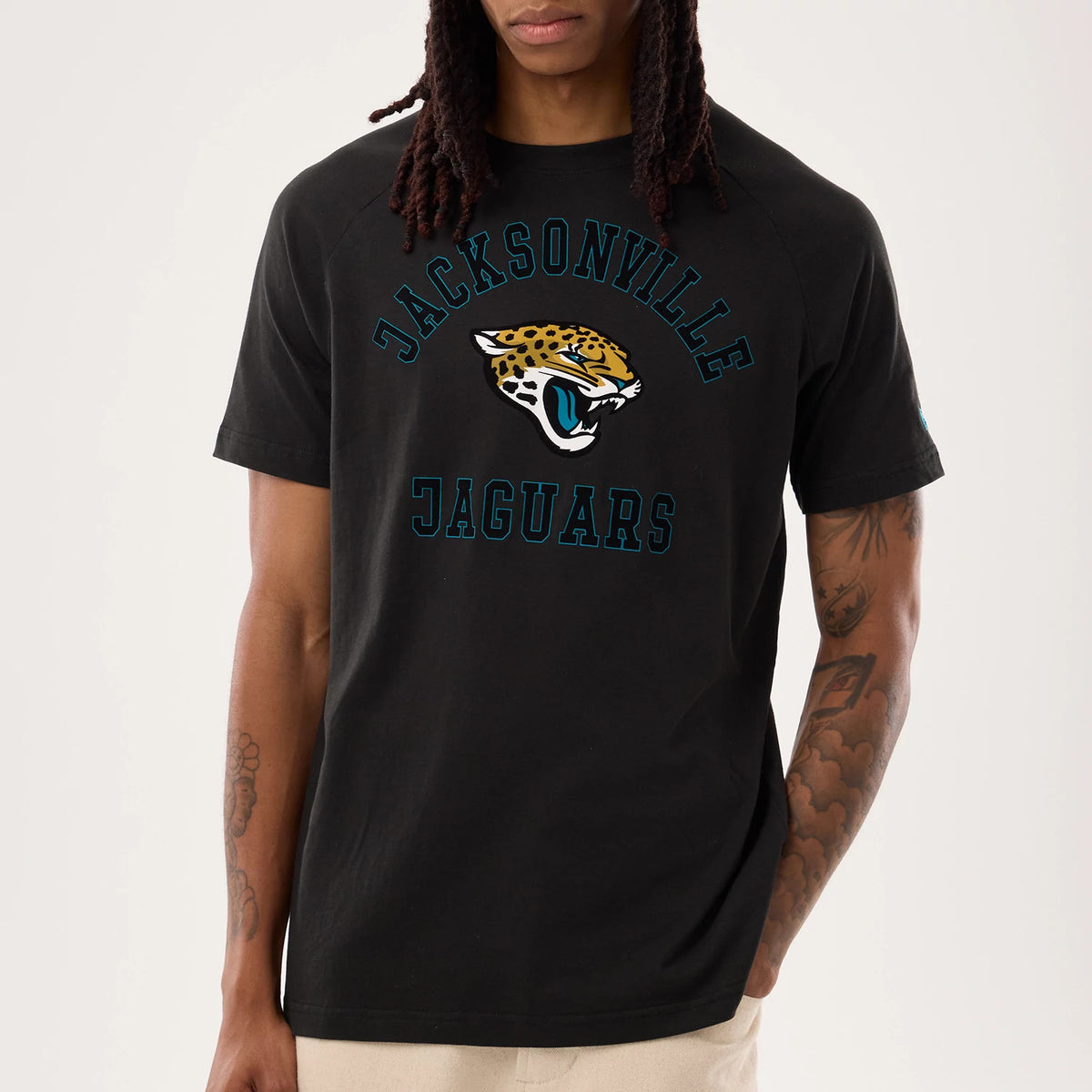 New Era Jacksonville Jaguars NFL Sideline 2026 Black T-Shirt, front view on a model with beige trousers, showcasing an embroidered Jacksonville Jaguars logo with a jaguar head in gold, black, white, and teal, framed by teal lettered embroidery.