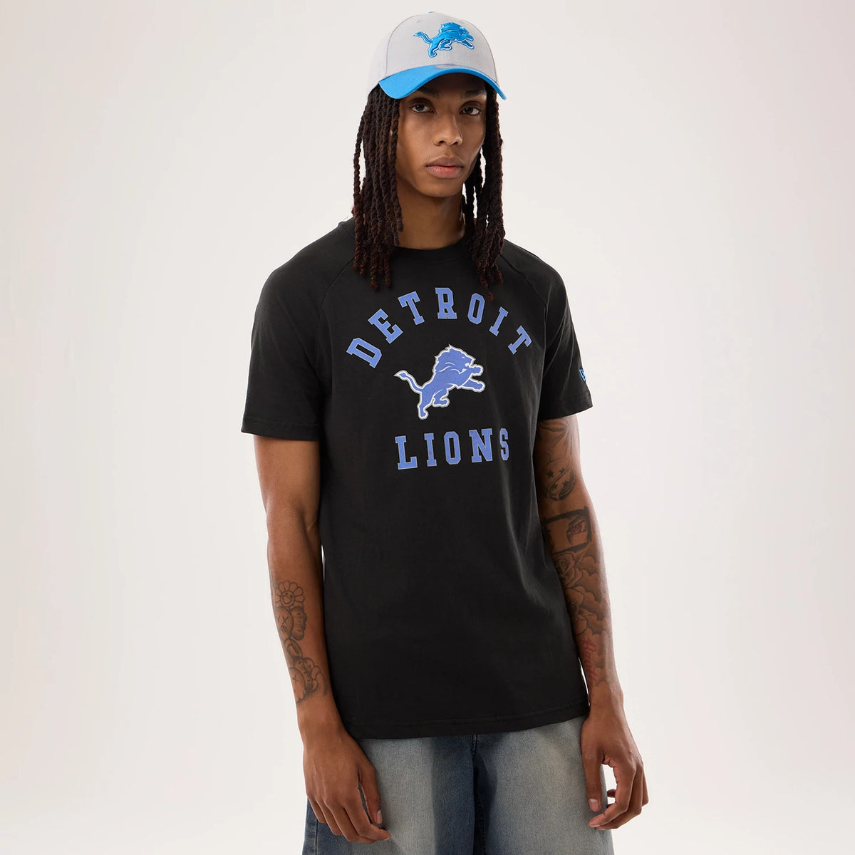 New Era Detroit Lions NFL Sideline 2026 Black T-Shirt, front view on-model showing the blue embroidered Detroit Lions logo centred on the chest, with matching lettering above and below, worn with a grey and blue cap featuring the team logo.