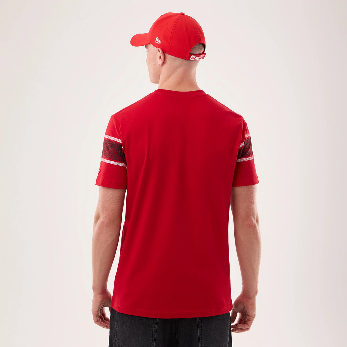 New Era Kansas City Chiefs NFL Sideline 2026 Red T-Shirt, back view on a model with a red cap, showing the plain red back with distinctive striped on the short sleeves and an embroidered New Era logo on the left sleeve.