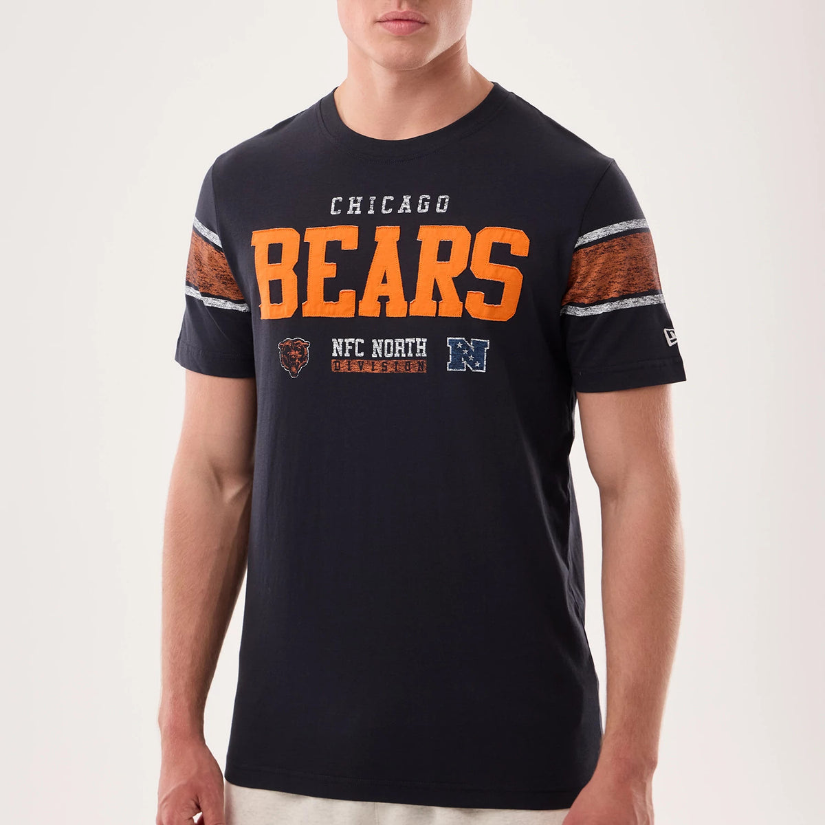 New Era Chicago Bears NFL Sideline 2026 Navy T-Shirt, front view on a model showing orange Bears lettering across the chest, embellished with embroidered Chicago and team logos below it, and contrasting striped panels on each sleeve.