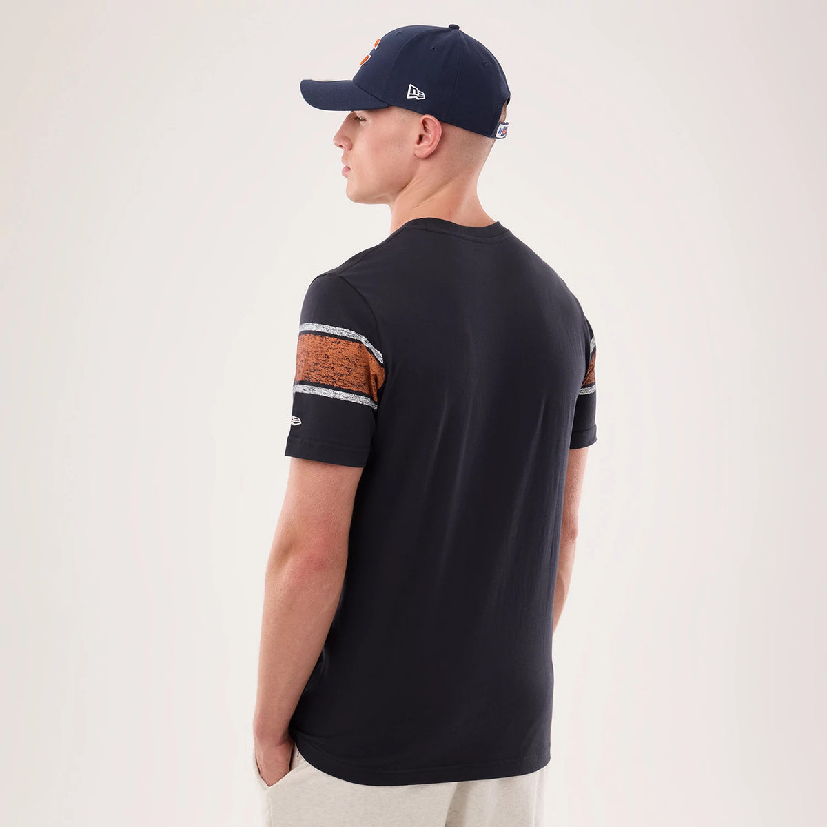 New Era Chicago Bears NFL Sideline 2026 Navy T-Shirt, back view on-model showing striped on the short sleeves, with orange and grey horizontal stripes, and a small embroidered New Era logo on the left sleeve, paired with a navy cap.