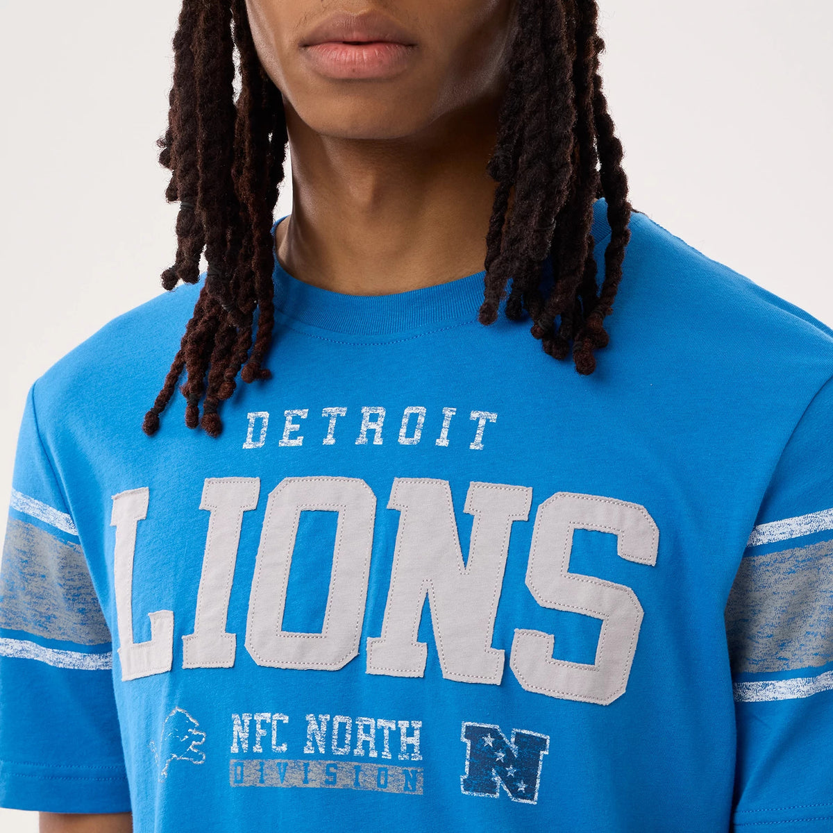 New Era Detroit Lions NFL Sideline 2026 Blue T-Shirt, front view on a model showing prominent white embroidered 'LIONS' lettering across the chest, with 'DETROIT' above and 'NFC NORTH' below, plus additional sleeve stripes in a distressed style.