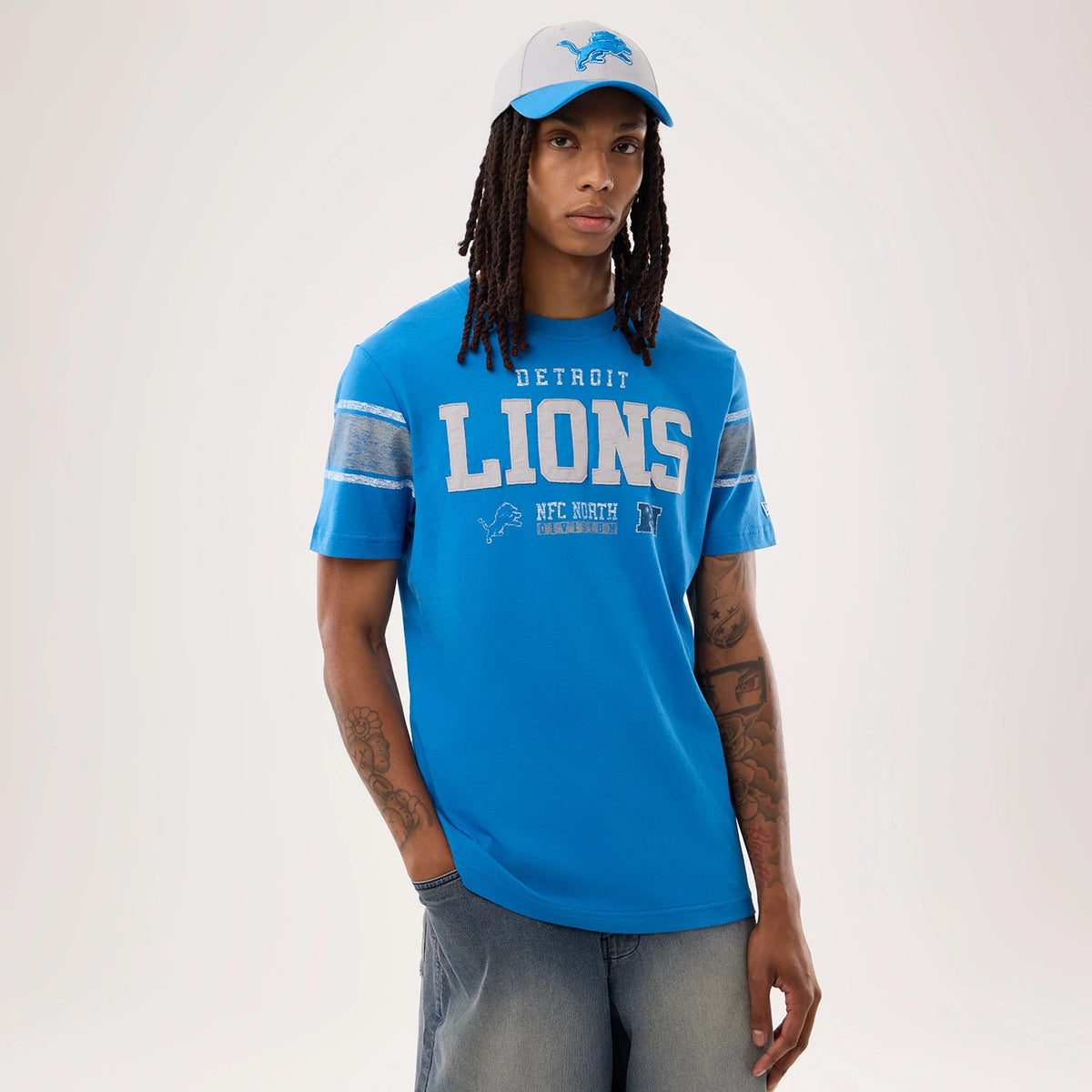New Era Detroit Lions NFL Sideline 2026 Blue T-Shirt, front view on a model paired with a cap, featuring large grey LIONS text across the chest, Detroit and NFC North graphics below, and highlighted grey bands on both sleeves.
