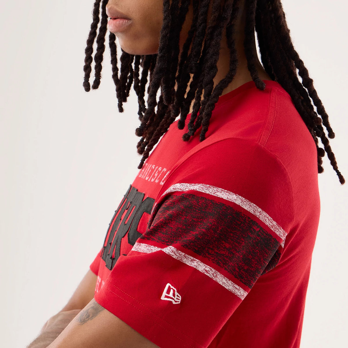 New Era San Francisco 49ers NFL Sideline 2026 Red T-Shirt, side view on a model showing glittery silver stripes and black textured details on the sleeve, with a small embroidered New Era logo above the sleeve cuff and San Francisco text on the chest.