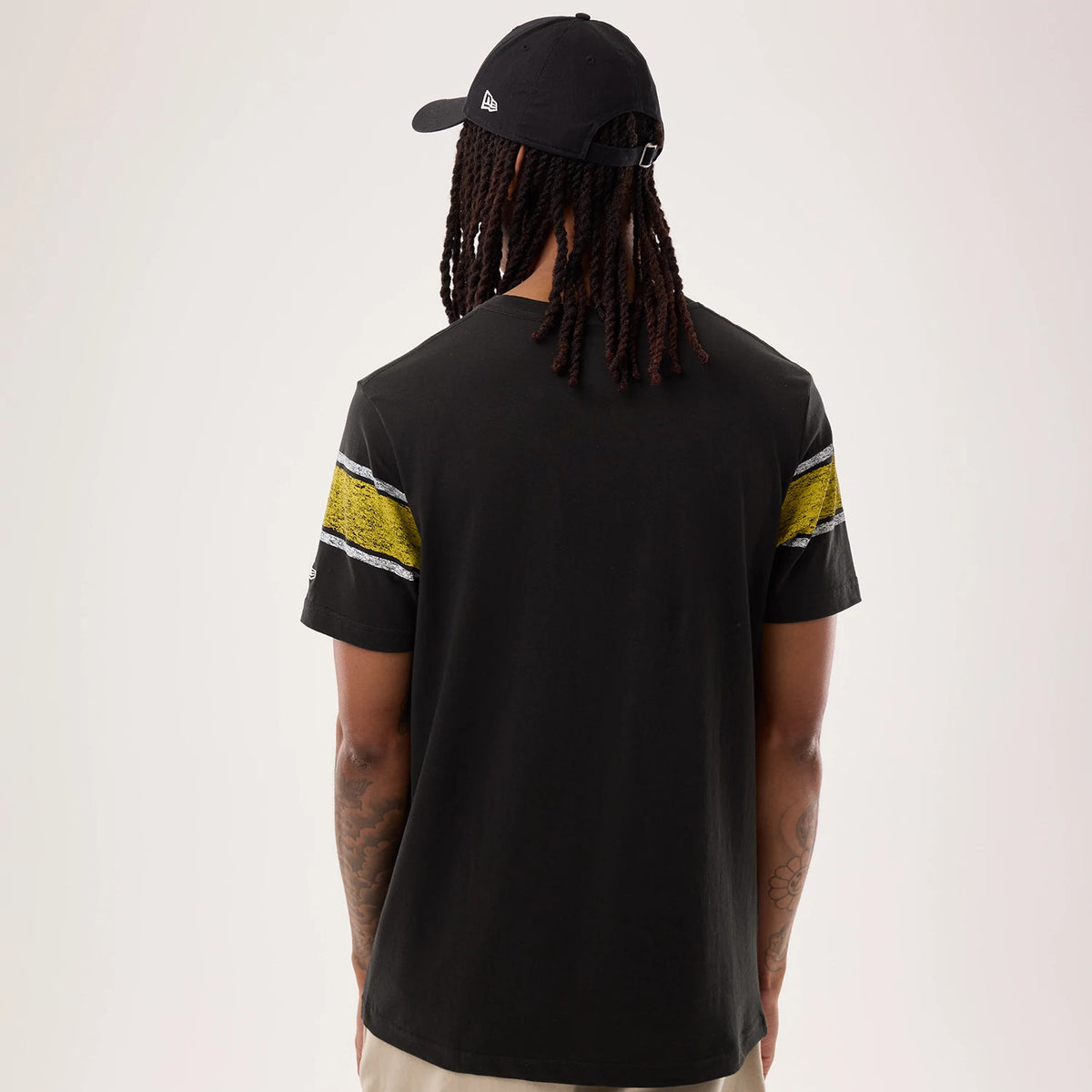 New Era Pittsburgh Steelers NFL Sideline 2026 Black T-Shirt, back view on a model with a black cap, showing a plain black back, distinctive yellow and white striped details on the sleeves, and a small embroidered New Era logo on the left sleeve.
