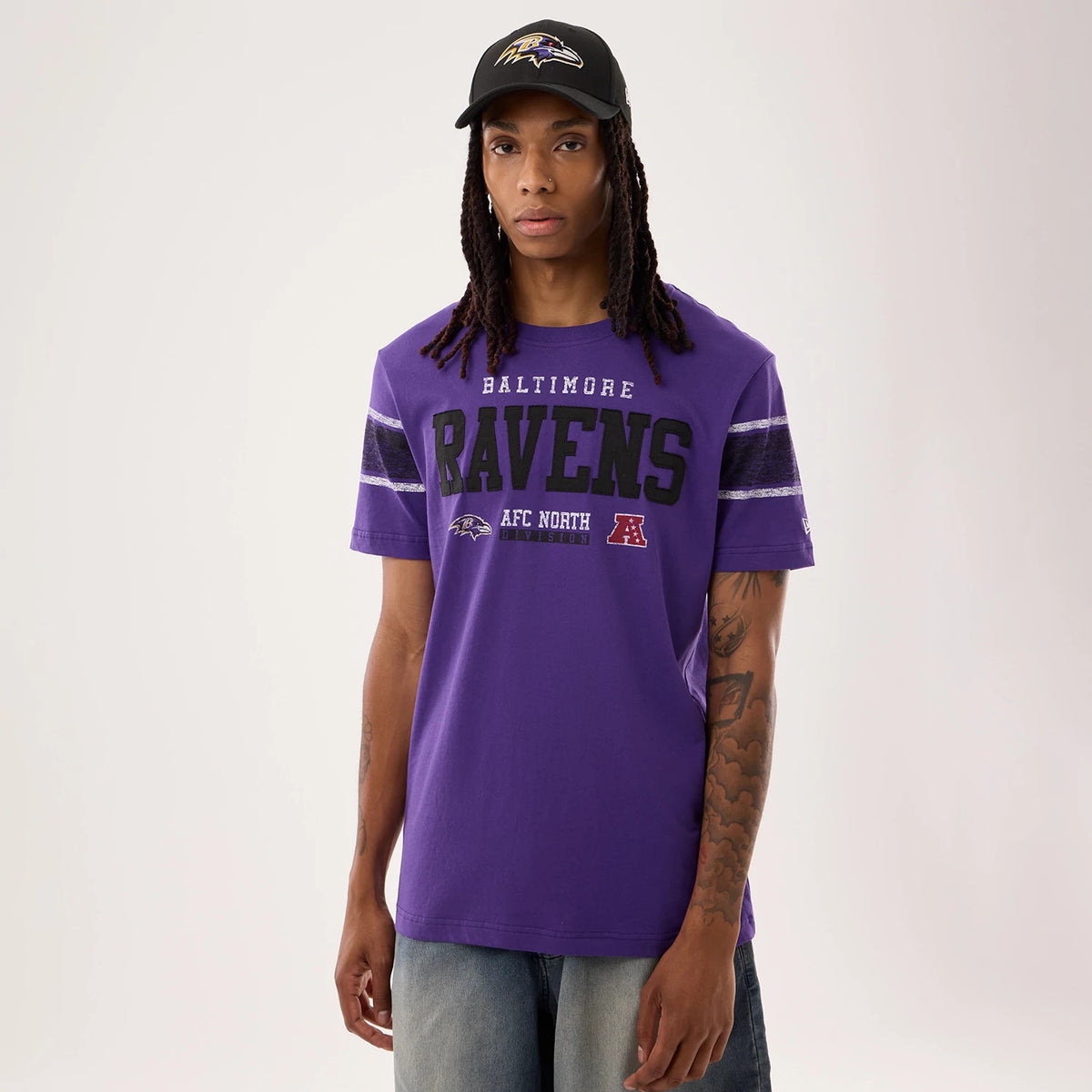 New Era Baltimore Ravens NFL Sideline 2026 Purple T-Shirt, front view on-model displaying black Ravens lettering across the chest, textured horizontal stripes on the sleeves, and a small embroidered New Era logo on the left sleeve.