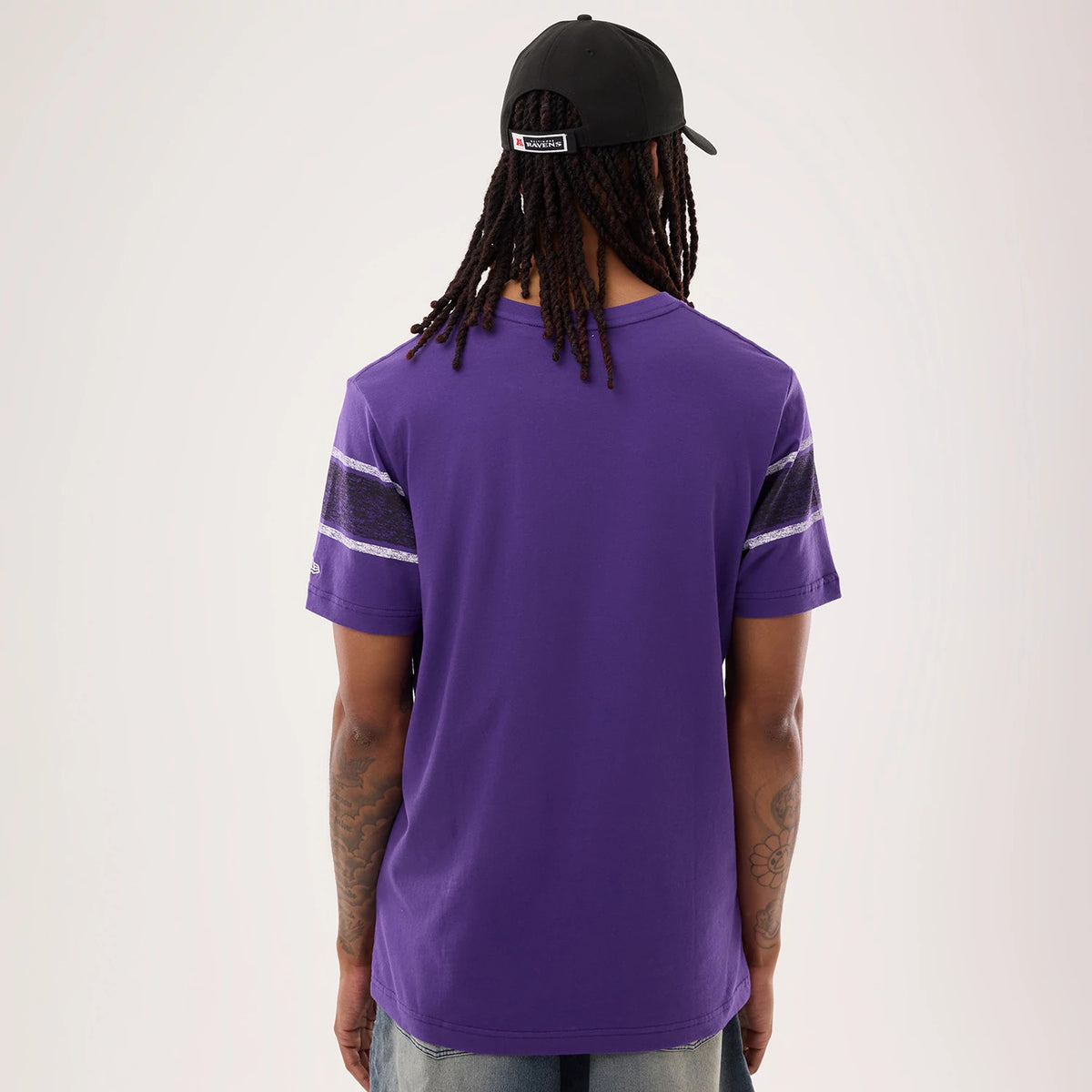 New Era Baltimore Ravens NFL Sideline 2026 Purple T-Shirt, back view on a model wearing jeans illustrating the solid purple colour with distinctive patterned stripes near the shoulders and sleeves, complemented by a sewn round neck design.