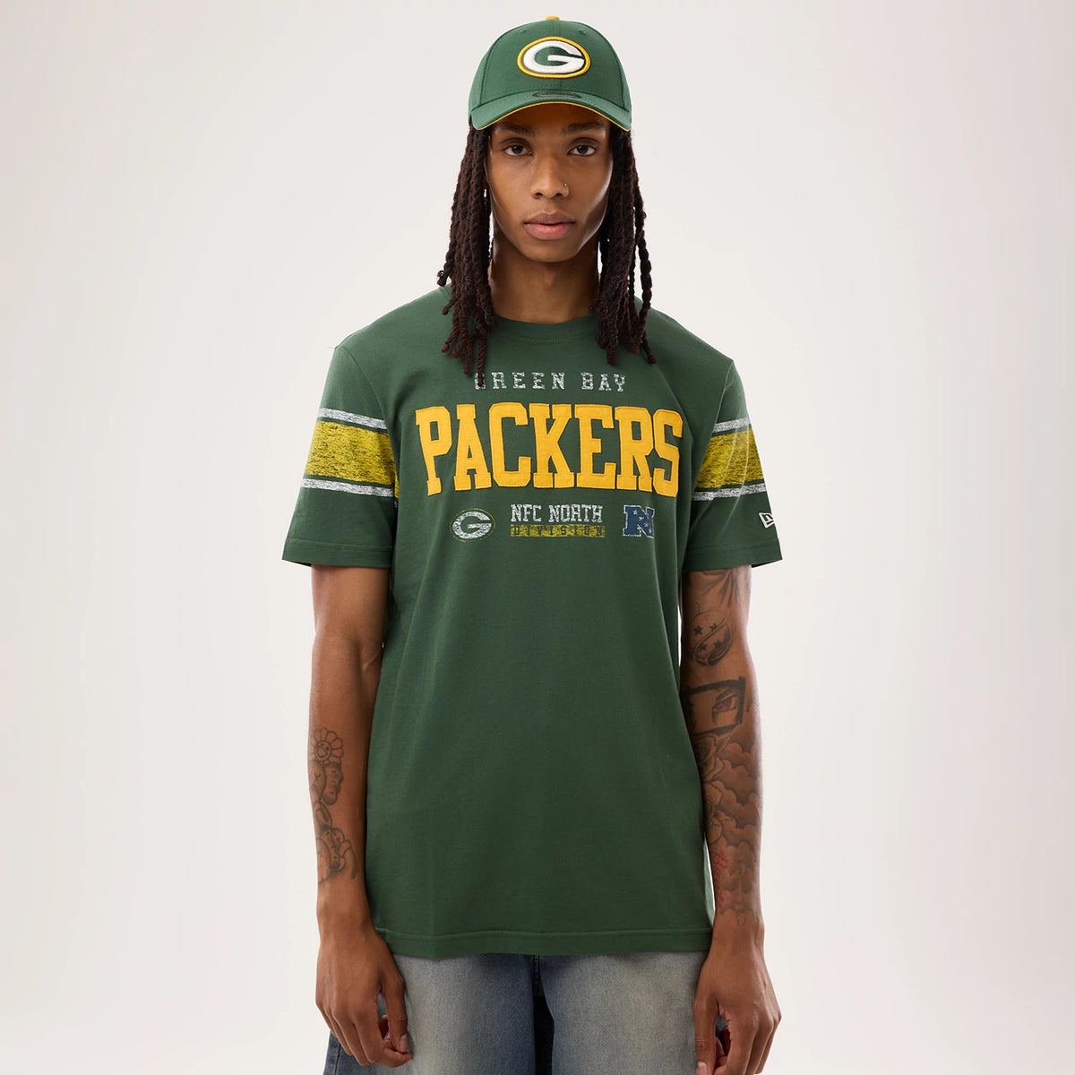 New Era Green Bay Packers NFL Sideline 2026 Dark Green T-Shirt, front view on a model wearing a matching cap, displaying the PACKERS lettering in yellow across the chest, green and yellow striped sleeves.