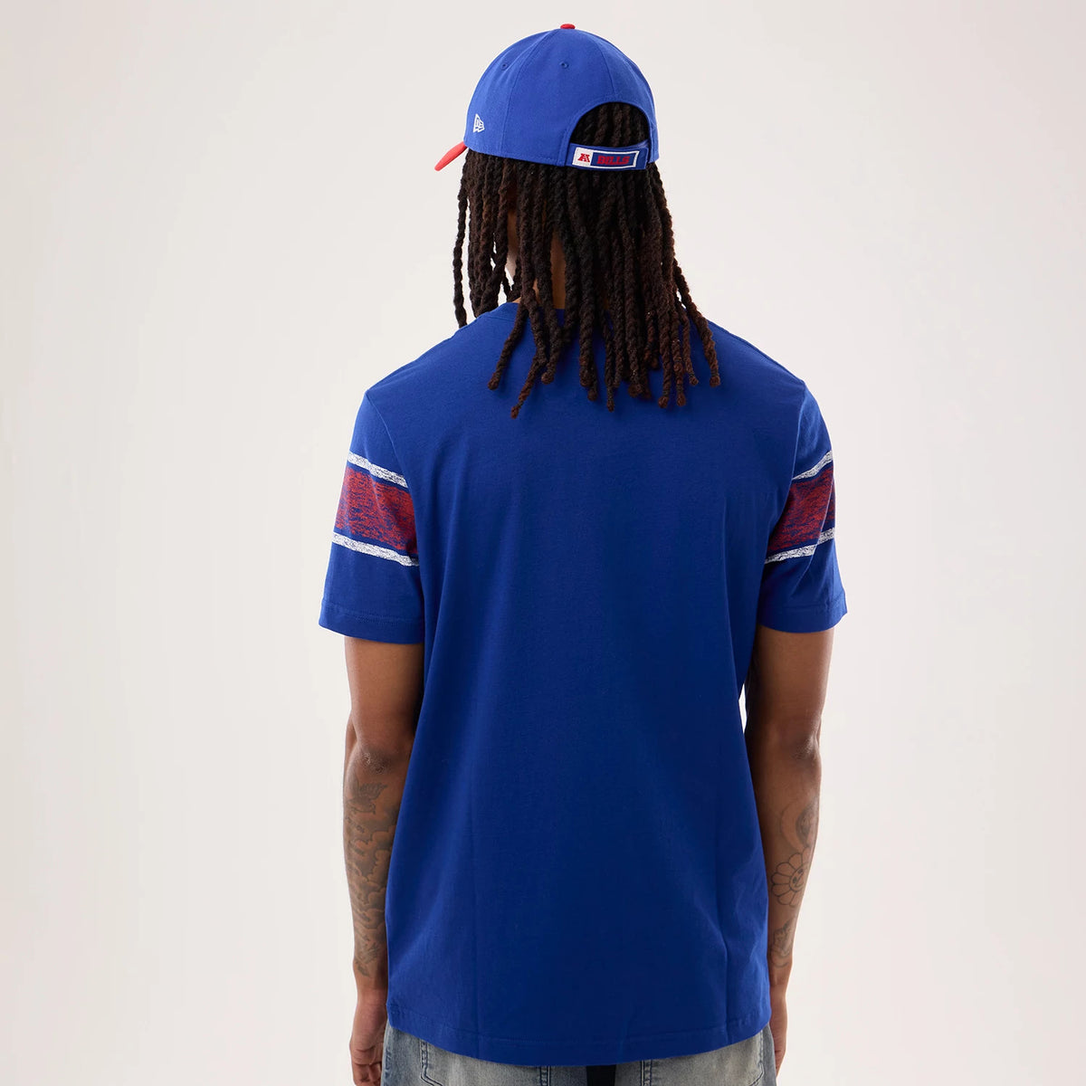 New Era Buffalo Bills NFL Sideline 2026 Blue T-Shirt, back view on a model wearing a blue cap, showing red and white graphic stripes on the sleeves, with a plain blue back that highlights simplicity and blue tone.