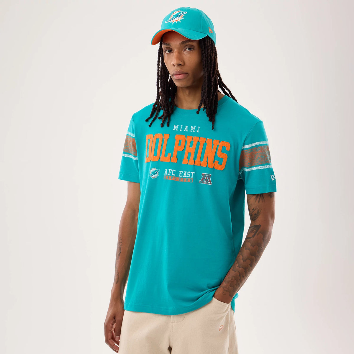 New Era Miami Dolphins NFL Sideline 2026 Turquoise T-Shirt, front view on-model featuring orange Dolphins lettering across the chest, accompanied by smaller Miami and AFC East details, with embroidered New Era logo on the left sleeve.