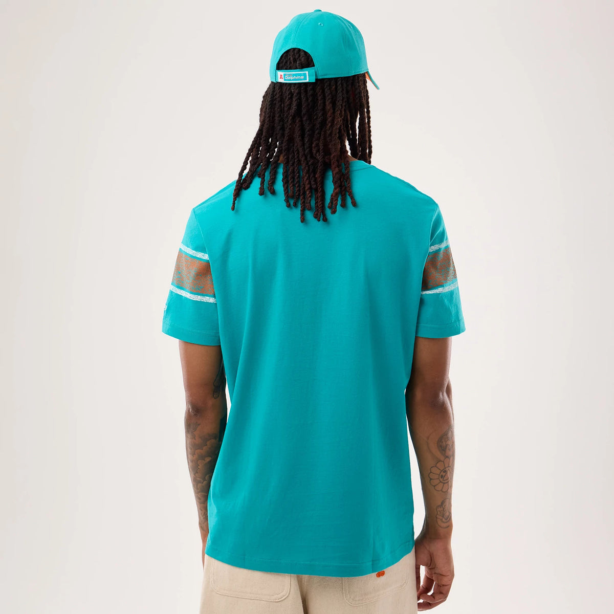 New Era Miami Dolphins NFL Sideline 2026 Turquoise T-Shirt, back view on a model wearing a matching cap showing a turquoise design with transparent sleeve panels and white stripes on the edges, highlighting a relaxed fit with short sleeves.