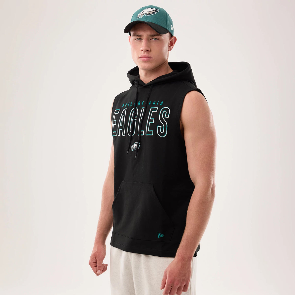 New Era Philadelphia Eagles NFL Sideline 2026 Black Tank Top, on-model view with an Eagles logo cap, featuring sleeveless design, large Eagles lettering across the chest in teal and white, and a kangaroo pocket.