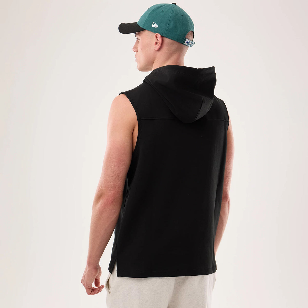 New Era Philadelphia Eagles NFL Sideline 2026 Black Tank Top, back view on a model wearing a green and black cap, showing the sleeveless design with a hood and relaxed fit, highlighting the plain black fabric of the top.