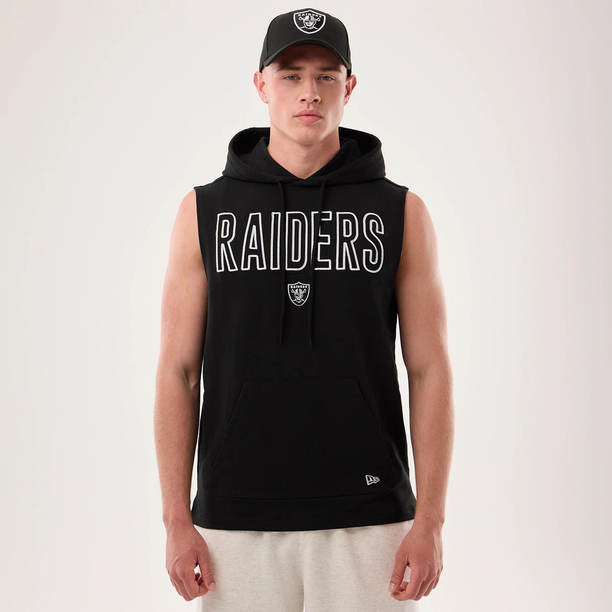 New Era Las Vegas Raiders NFL Sideline 2026 Black Tank Top, front view on a model wearing a matching cap, featuring white Raiders logo lettering across the chest, a small embroidered logo below it, and an additional New Era logo near the hem.