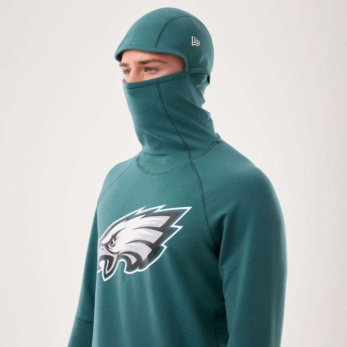 New Era Philadelphia Eagles NFL Sideline 2026 Dark Green Balaclava Hoodie, three-quarter view on-model highlighting the integrated balaclava design, a prominent white and grey Eagles logo printed on the chest.