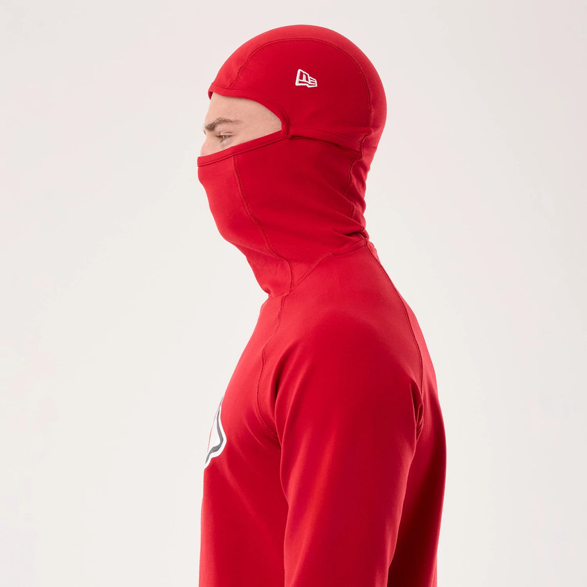 New Era Kansas City Chiefs NFL Sideline 2026 Red Balaclava Hoodie, side view showing a close-fitting red balaclava style hood, an embroidered New Era logo on the side of the head, and a glimpse of a team graphic on the chest.