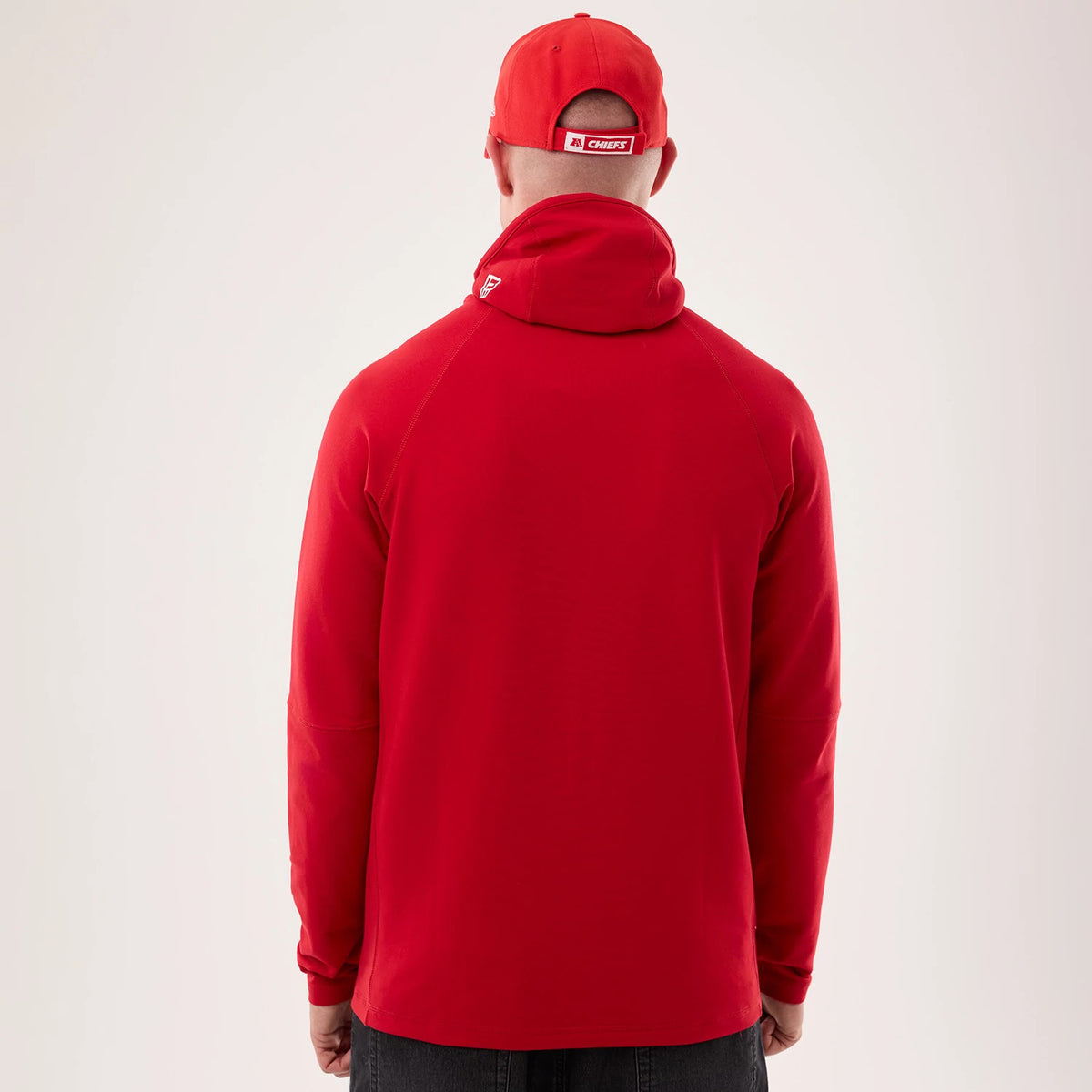 New Era Kansas City Chiefs NFL Sideline 2026 Red Balaclava Hoodie, back view on-model showing a deep red colour with a high, rolled collar design, a small raised New Era logo on the collar, and a matching red cap worn by the model.