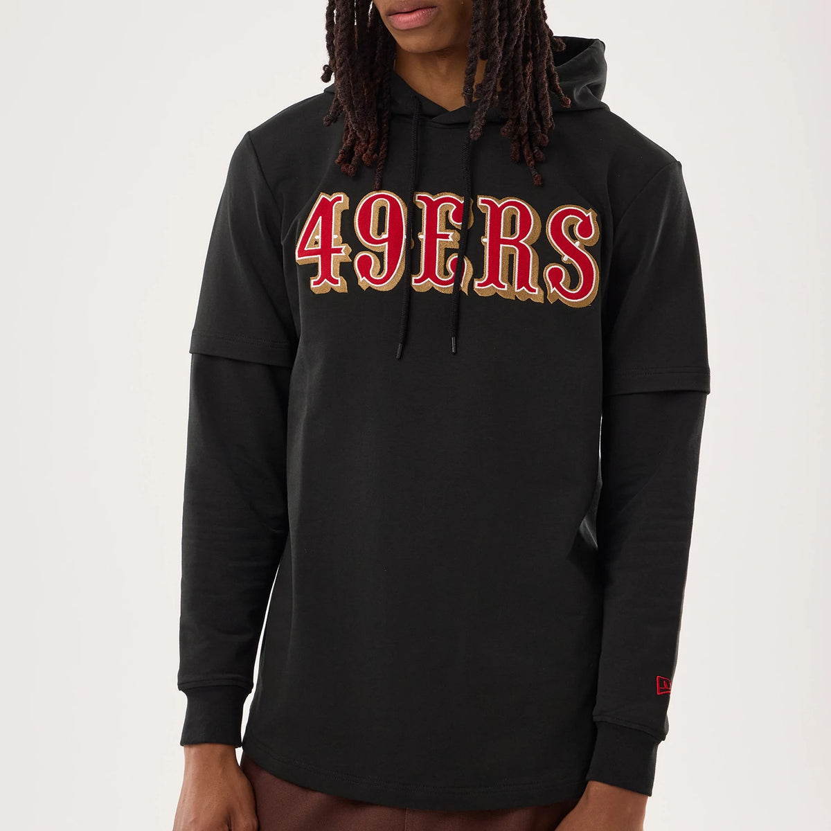 New Era San Francisco 49ers NFL Sideline 2026 Black Double Sleeve Hoodie, front view on a model featuring large embroidered red and gold 49ERS lettering across the chest, layered sleeves, and a red embroidered New Era flag logo on the left cuff.