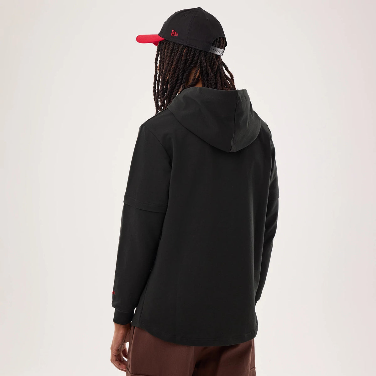 New Era San Francisco 49ers NFL Sideline 2026 Black Double Sleeve Hoodie, back view on a model wearing a black cap with a red visor, featuring a relaxed fit with a hood and double-layer sleeves, along with team branding on one sleeve.