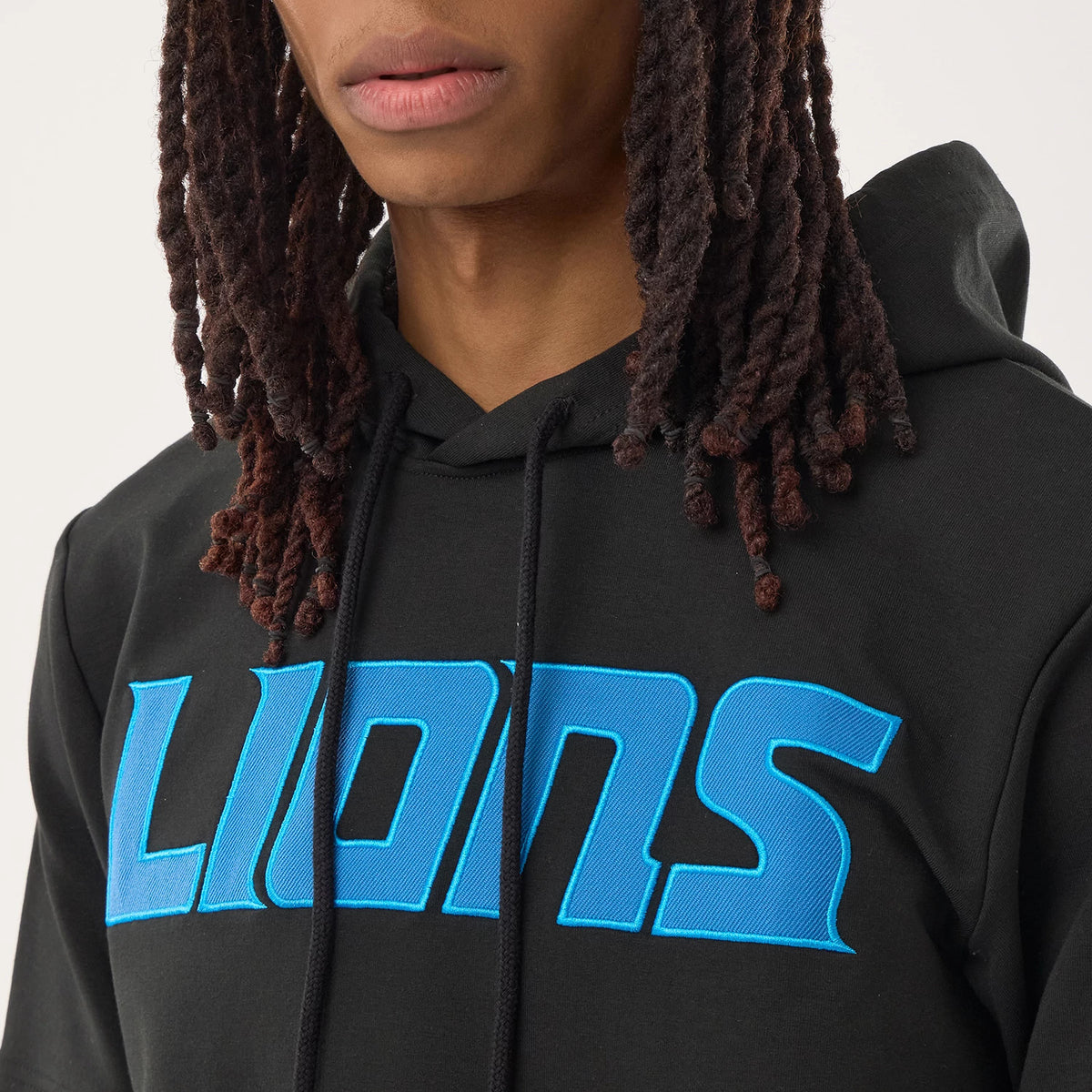 New Era Detroit Lions NFL Sideline 2026 Black Double Sleeve Hoodie, front view on a model, showing a blue embroidered 'LIONS' logo across the chest, a black drawstring on the hood, and a close-up of the double layered sleeves.