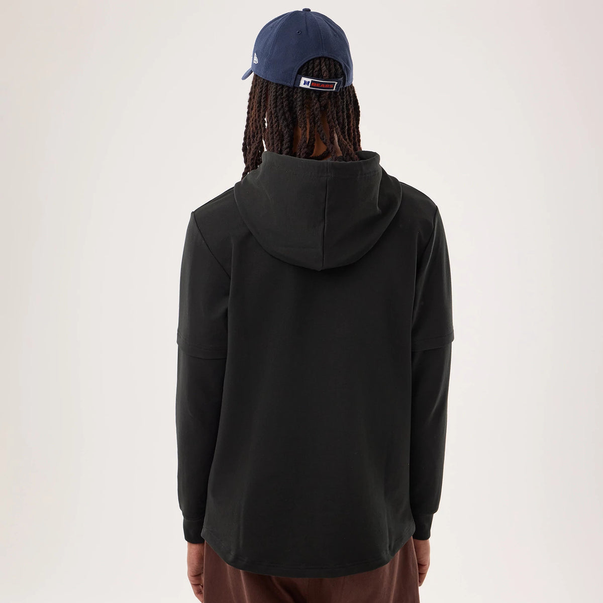 New Era Chicago Bears NFL Sideline 2026 Black Double Sleeve Hoodie, back view on-model showcasing the plain black back with a roomy hood, the double sleeve construction at the arms, and a relaxed fit over brown trousers.