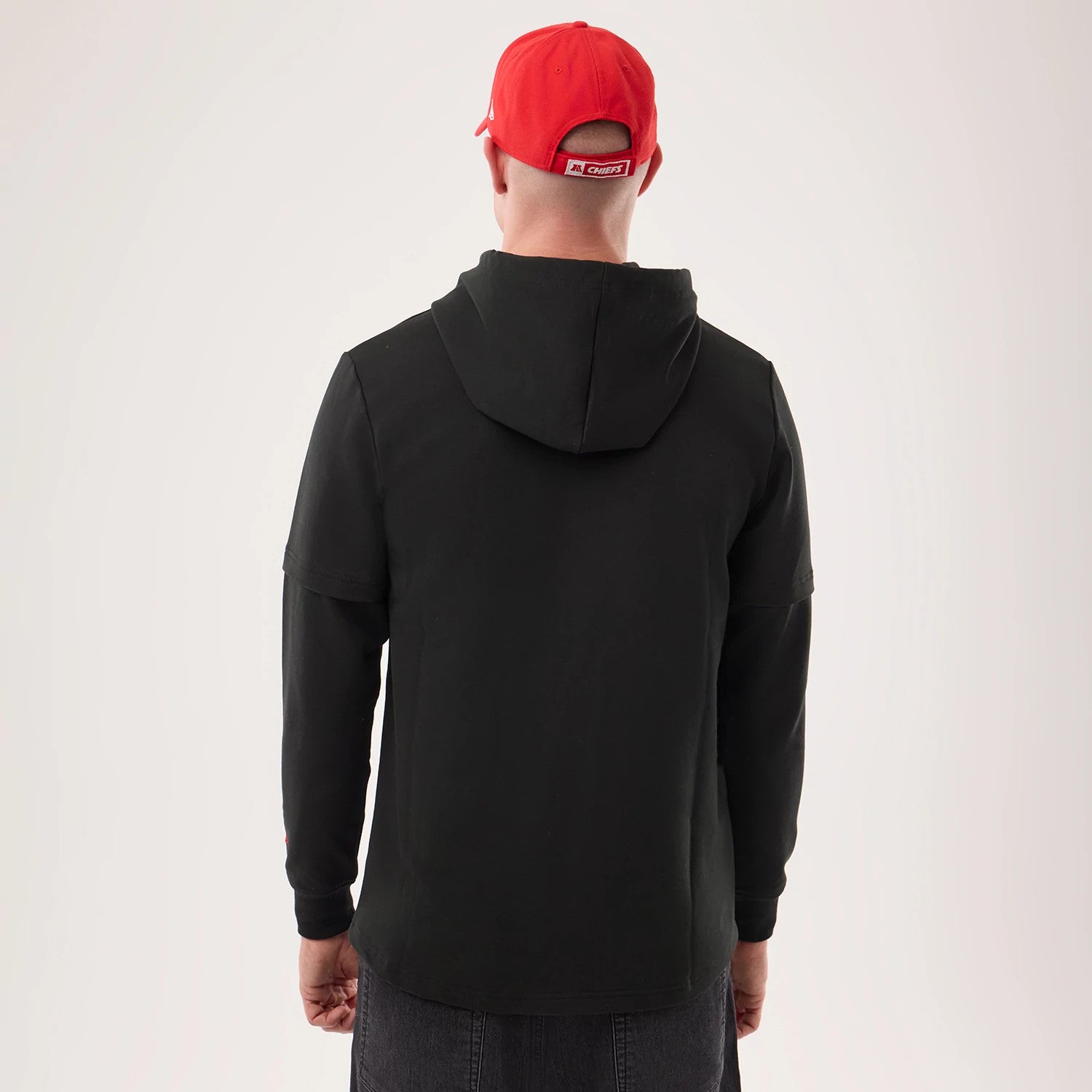 New Era Kansas City Chiefs NFL Sideline 2026 Black Double Sleeve Hoodie, back view on a model with a red cap, shows the black hoodie design with a double sleeve detail, a relaxed fit and the concise hood adorning the upper back.