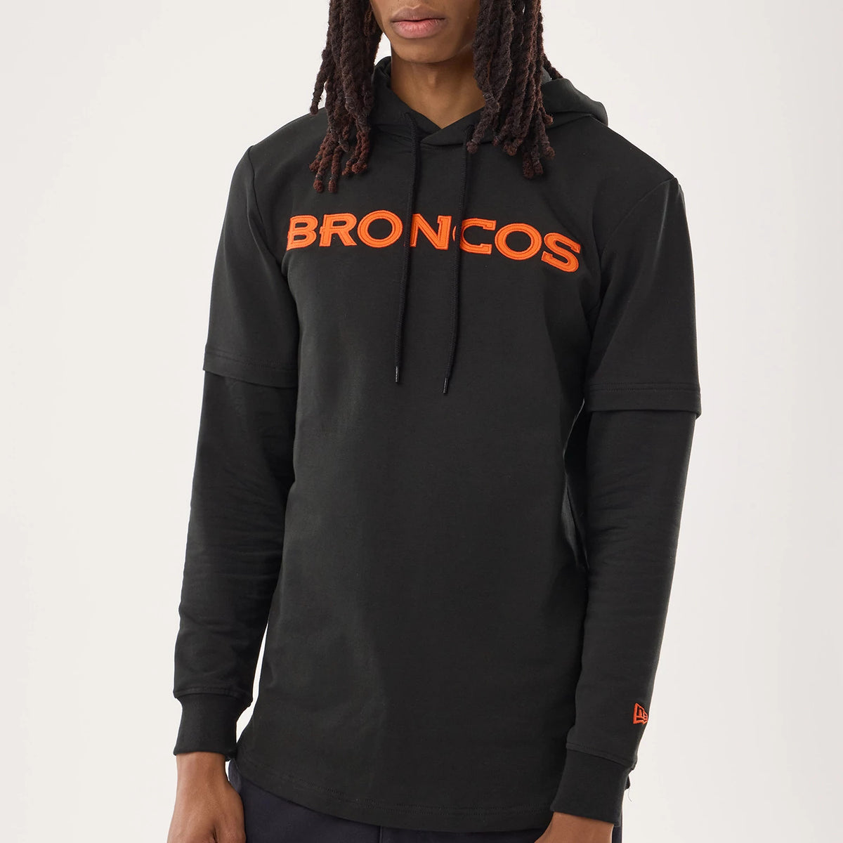 New Era Denver Broncos NFL Sideline 2026 Black Double Sleeve Hoodie, front view on a model showing the orange Broncos lettering across the chest, a double-layer sleeve design, and an embroidered New Era logo above the left cuff.