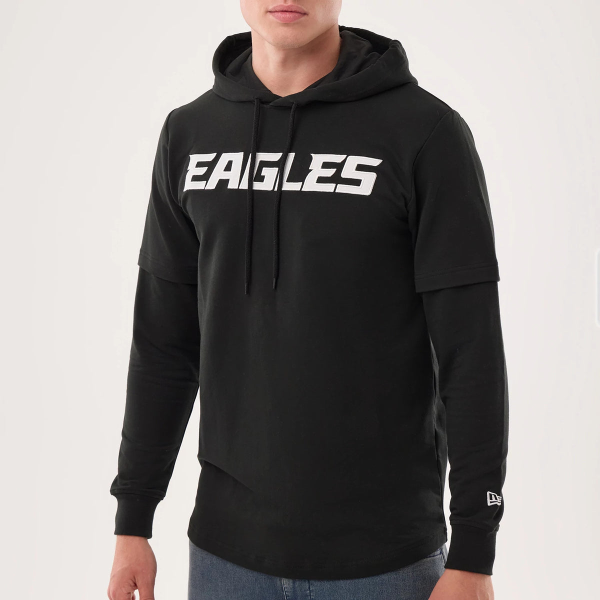 New Era Philadelphia Eagles NFL Sideline 2026 Black Double Sleeve Hoodie, front view on-model featuring white Eagles text across the chest, a double-layered sleeve with a printed New Era logo on one wrist, and a hood with black drawstrings.