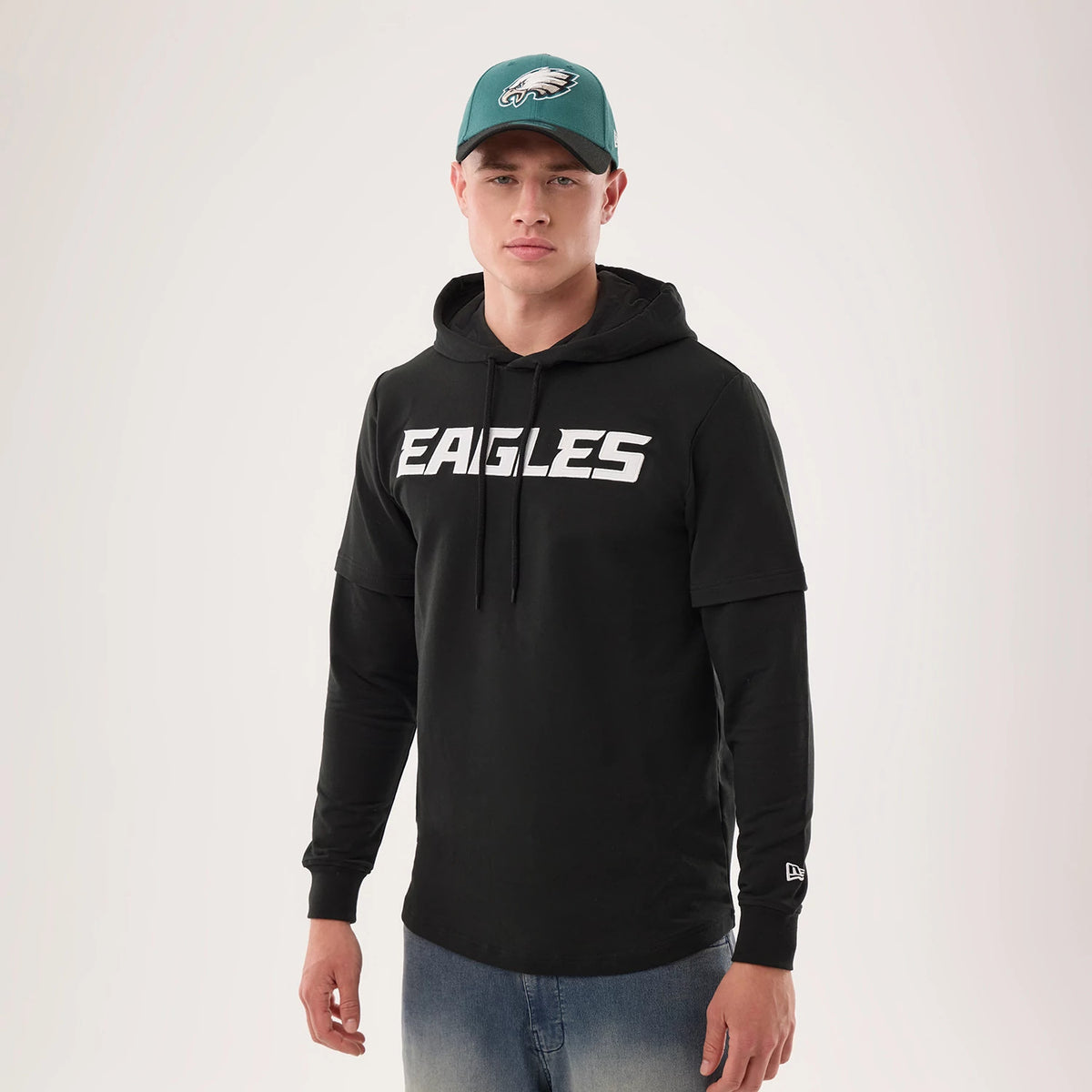 New Era Philadelphia Eagles NFL Sideline 2026 Black Double Sleeve Hoodie, front view on-model showing white Eagles lettering across the chest, layered sleeve design with a small printed New Era logo near the cuff and a black drawstring hood.