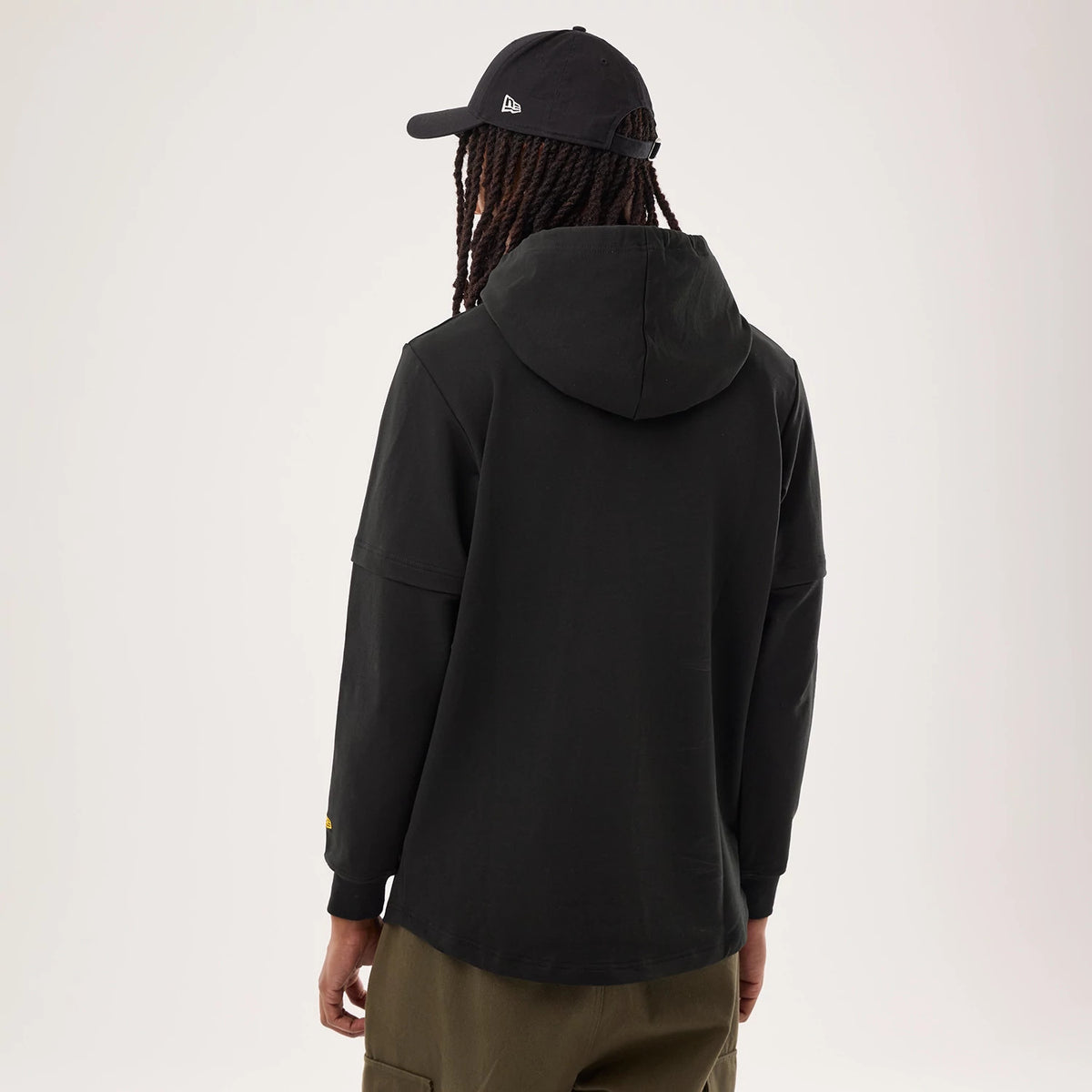 New Era Pittsburgh Steelers NFL Sideline 2026 Black Double Sleeve Hoodie, back view on-model showing the hood laying flat against the shoulders, dropped shoulder seams, a small yellow embroidered logo on the left sleeve, styled with a black cap.