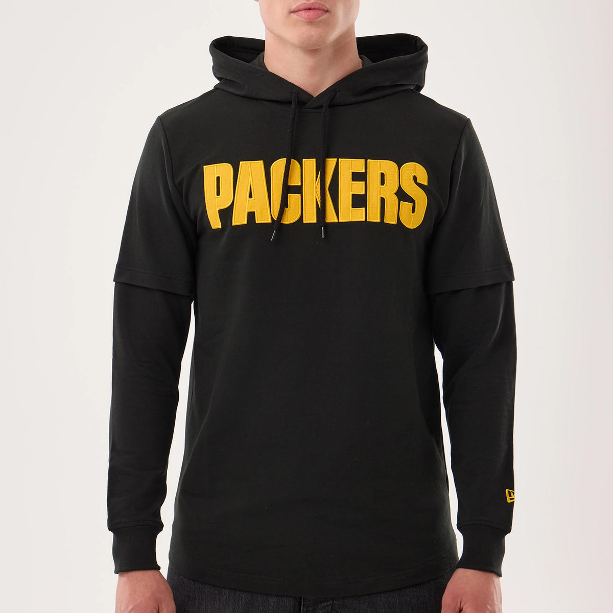 New Era Green Bay Packers NFL Sideline 2026 Black Double Sleeve Hoodie, front view on-model showing yellow embroidered PACKERS text across the chest, hoodie with drawstrings, layered sleeve design, and a small embroidered New Era logo on the cuff.