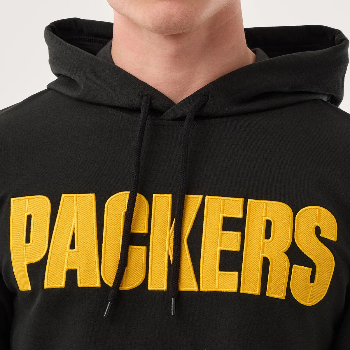 New Era Green Bay Packers NFL Sideline 2026 Black Double Sleeve Hoodie, front view showing the embroidered Packers lettering in yellow across the chest, a drawstring hood framing the neck, and worn by a model for a casual look.