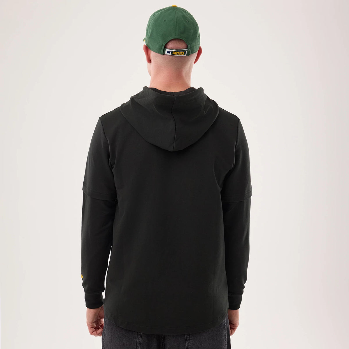 New Era Green Bay Packers NFL Sideline 2026 Black Double Sleeve Hoodie, back view on a model highlighting the hood draped down the upper back, double sleeve design, and a small embroidered team logo on the lower sleeve.