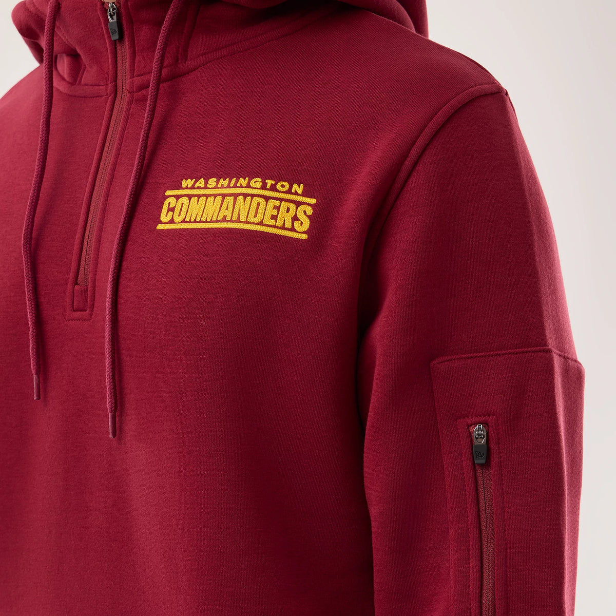 New Era Washington Commanders NFL Sideline 2026 Dark Red Pullover Hoodie, front view showing the embroidered yellow Washington Commanders logo on the left chest, a drawstring hood with cords, and a small zipped pocket on the upper left sleeve.