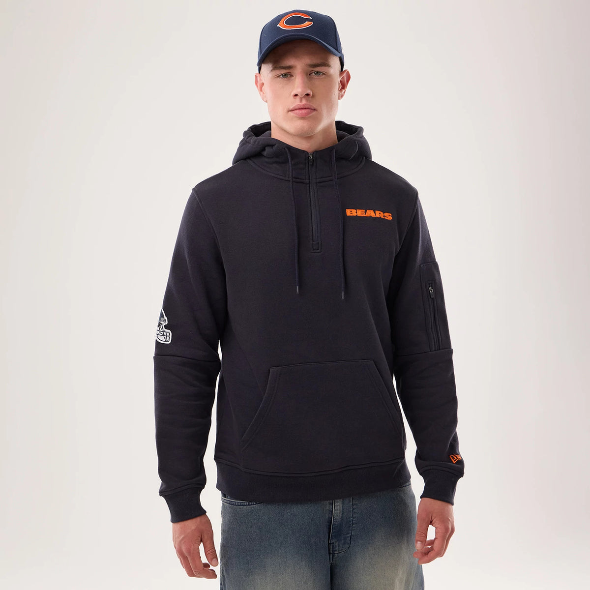 New Era Chicago Bears NFL Sideline 2026 Navy Pullover Hoodie, front view on-model with a navy hood, orange Bears lettering on the chest, an embroidered team logo on the left sleeve, and a small pocket on the right arm.