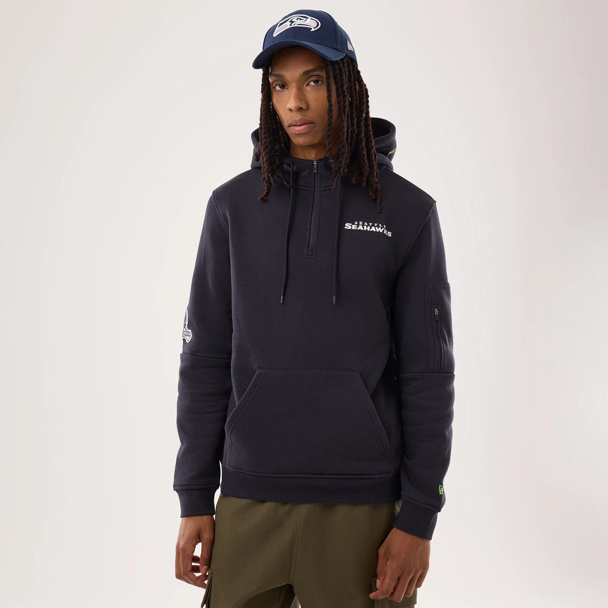 New Era Seattle Seahawks NFL Sideline 2026 Navy Pullover Hoodie, front view on-model showing the navy hoodie with an embroidered Seattle Seahawks logo on the left chest, a pocket with zip detail on the sleeve, and a hood with drawstrings.