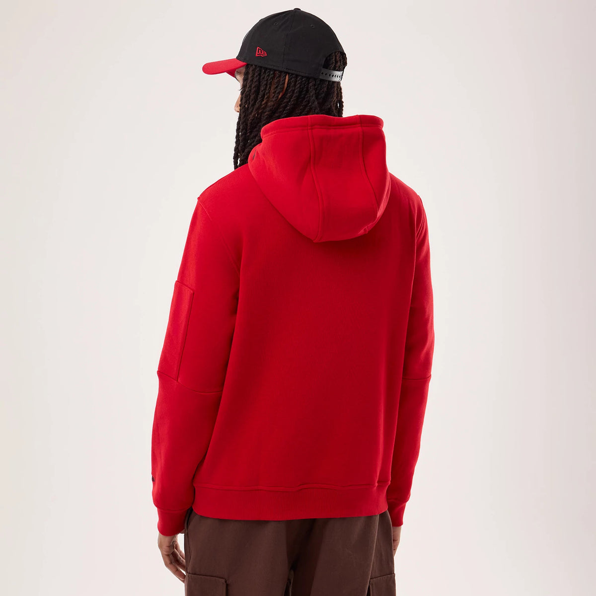 New Era San Francisco 49ers NFL Sideline 2026 Red Pullover Hoodie, back view on a model wearing a black and red cap, showing the hoodie’s relaxed fit with a spacious hood and plain red back, cuffs, and hemline creating a clean silhouette.