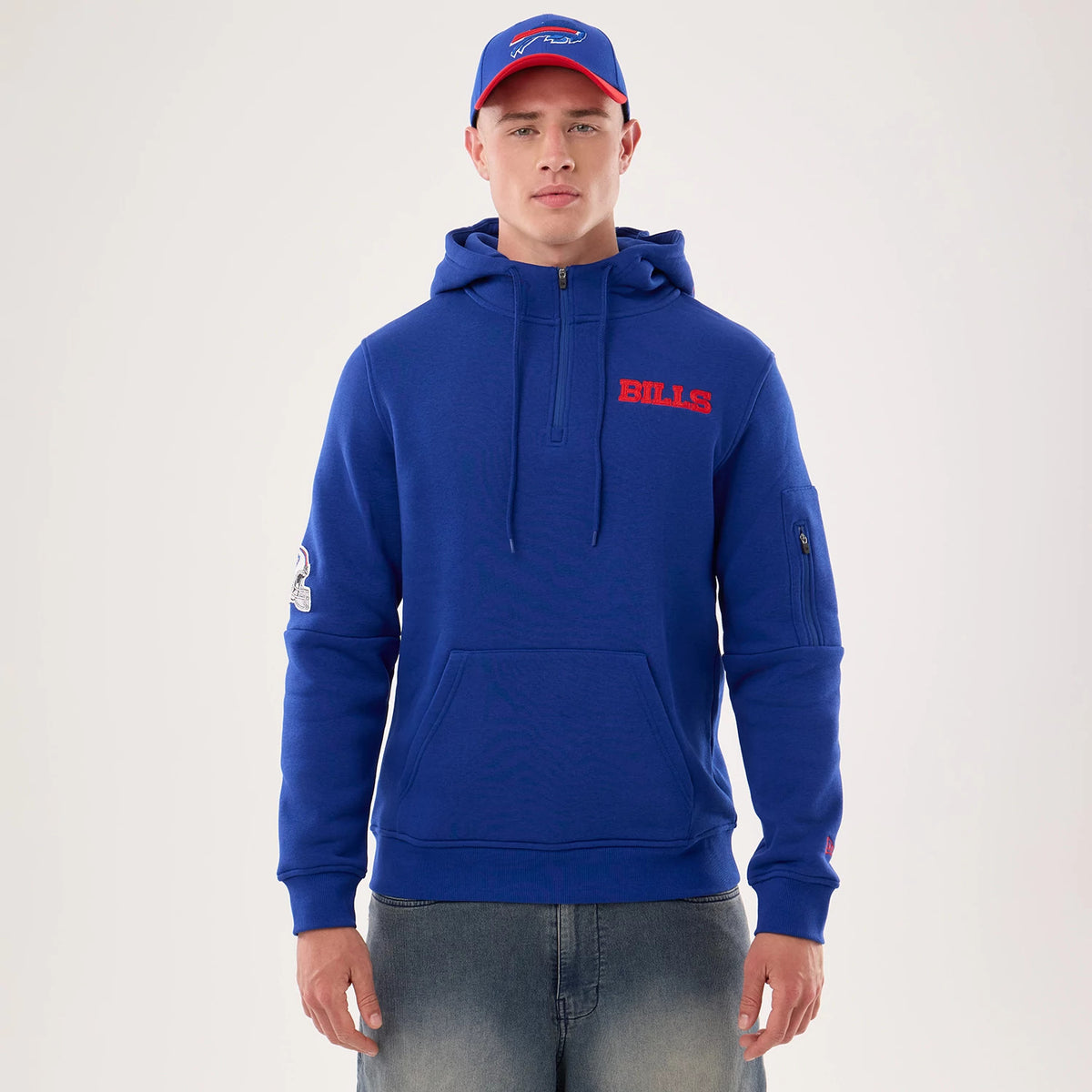 New Era Buffalo Bills NFL Sideline 2026 Blue Pullover Hoodie, front view on a model with a blue cap, featuring an embroidered red BILLS logo on the chest, a small Bills logo on the sleeve, and a half-zip with a hood.