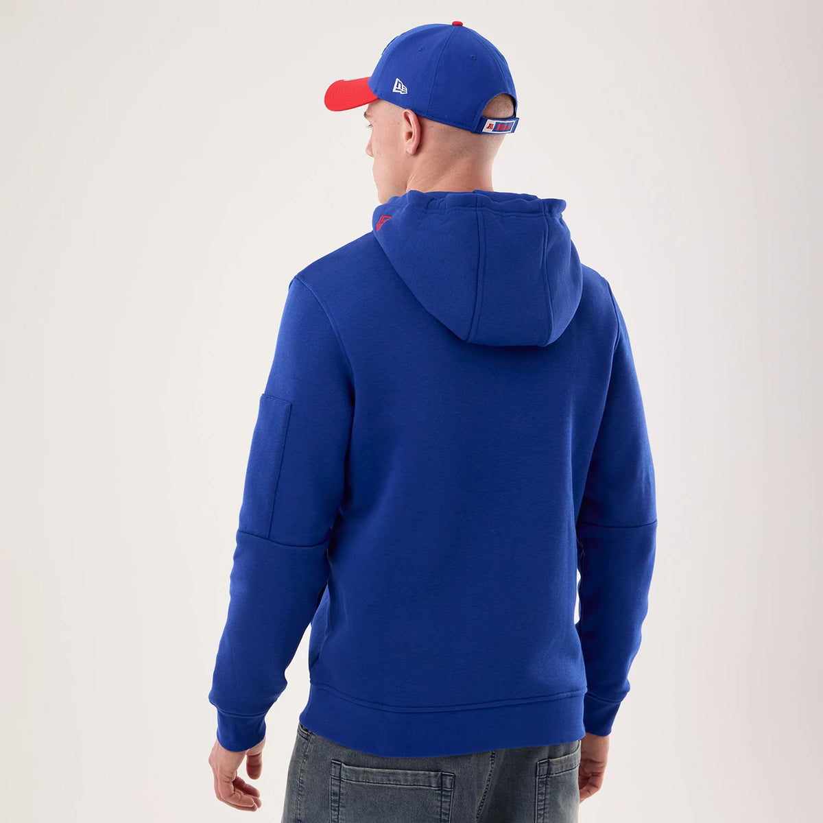 New Era Buffalo Bills NFL Sideline 2026 Blue Pullover Hoodie, back view on-model showing the rich blue fabric with a hood, pocket on the sleeve, and paired with a matching blue cap featuring the debossed New Era logo on the side.
