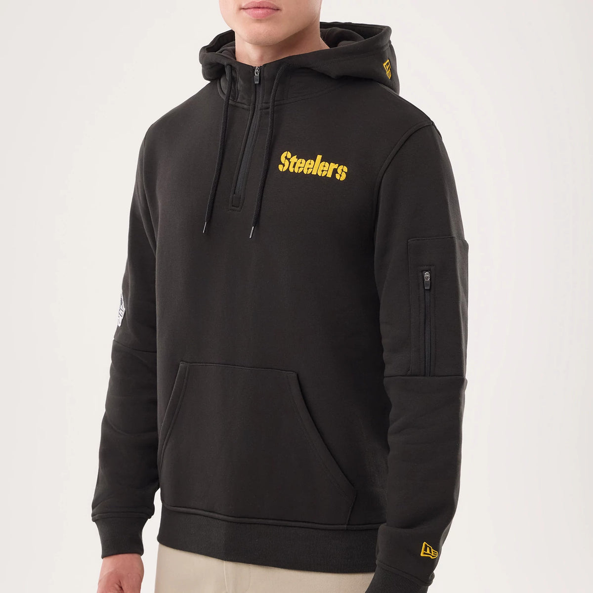 New Era Pittsburgh Steelers NFL Sideline 2026 Black Pullover Hoodie, three-quarter view showcasing the yellow embroidered Steelers wordmark on the chest, a sleeve pocket with a zip on the left arm, and the New Era logo on the left cuff.