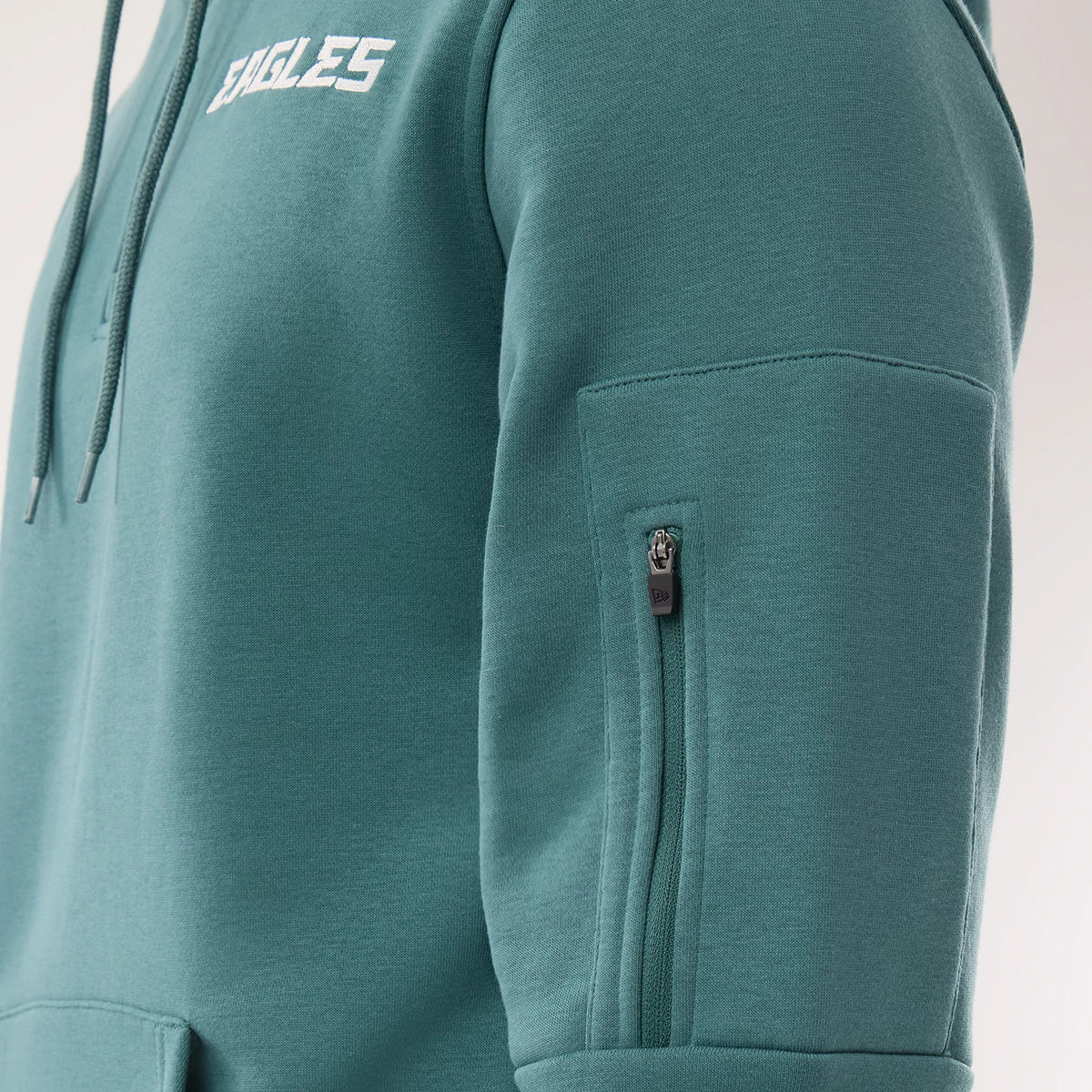 New Era Philadelphia Eagles NFL Sideline 2026 Dark Green Pullover Hoodie, three-quarter view highlighting the white embroidered Eagles logo on the chest, drawstrings hanging from the hood, and a zip pocket with a New Era logo on the upper sleeve.