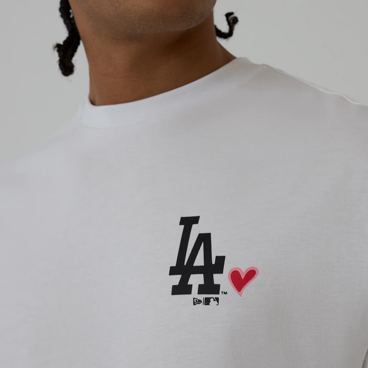 New Era LA Dodgers MLB Heart Graphic White T-Shirt, front view showing the black printed LA logo paired with a small red heart on the left chest, worn by a model, featuring a crew neck design.