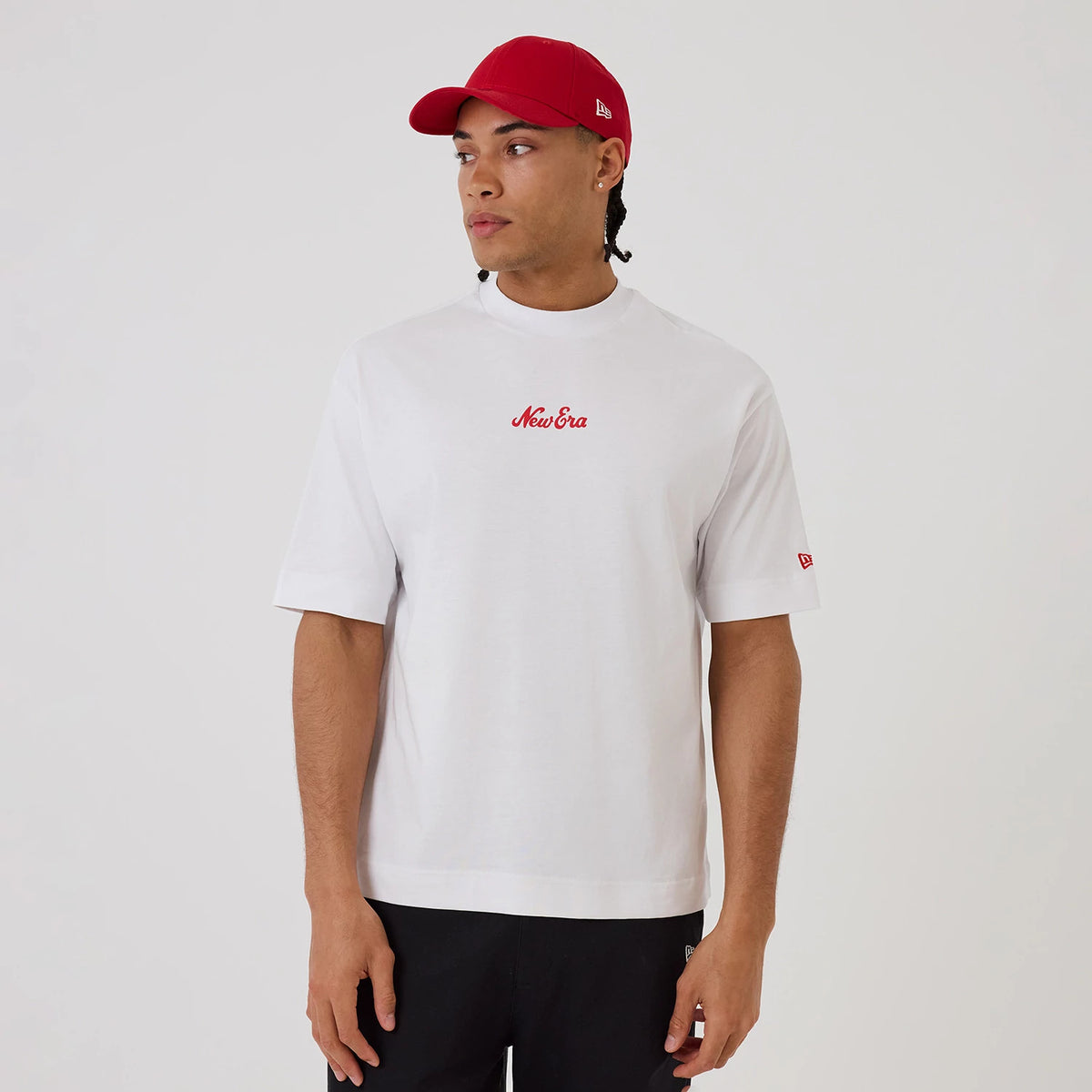 New Era Love Graphic White T-Shirt, front view on-model showing the red embroidered New Era script logo on the chest, with a red New Era flag embroidered on the left sleeve and styled with a red cap and black trousers.