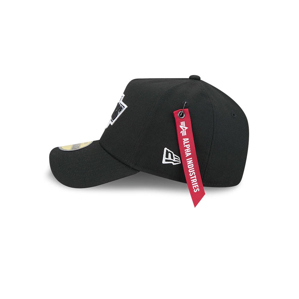 LA Kings NHL X Alpha Black New Era 59FORTY A-Frame Fitted Cap, side view showing the red Alpha Industries tag hanging from the rear panel, the New Era flag logo embroidered on the left side and a black curved visor with a 59FORTY size sticker.