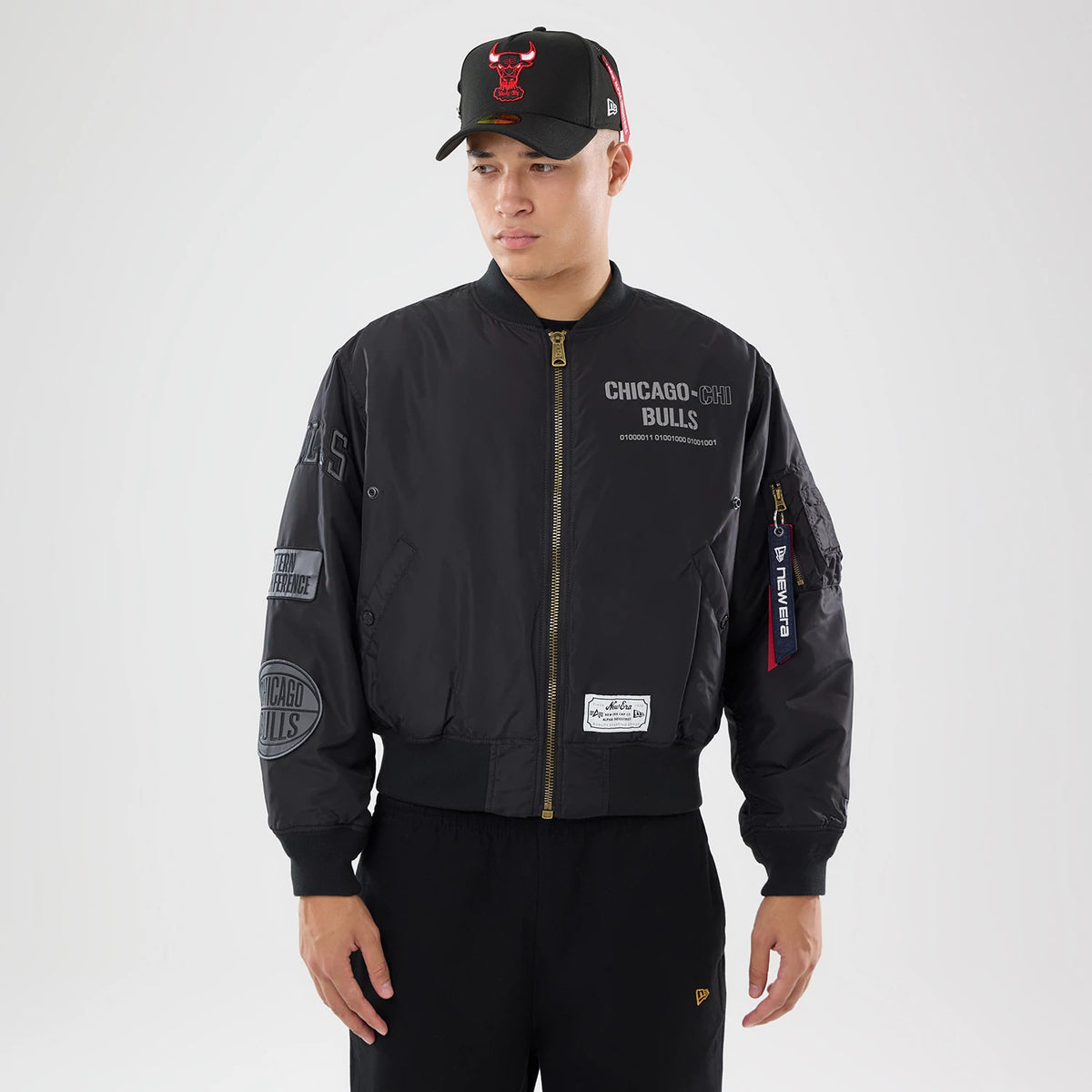 New Era Chicago Bulls NBA X Alpha Black Bomber Jacket & Tactical Vest, front view on-model showing the grey embroidered Chicago Bulls logo on the chest, zip closure down the centre, and New Era branding on a red tag hanging from the sleeve pocket.