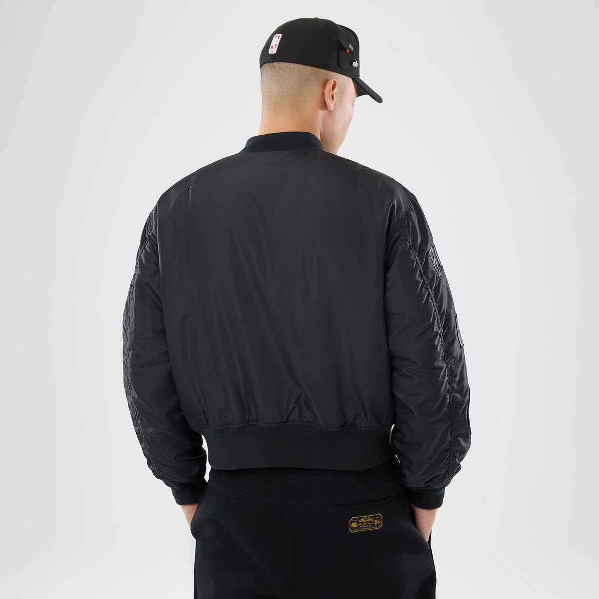 New Era Chicago Bulls NBA X Alpha Black Bomber Jacket & Tactical Vest, back view on-model featuring a black finish, ribbed hem and cuffs, quilted detail on sleeves, and branding details, complemented by a matching black cap with an embroidered logo.