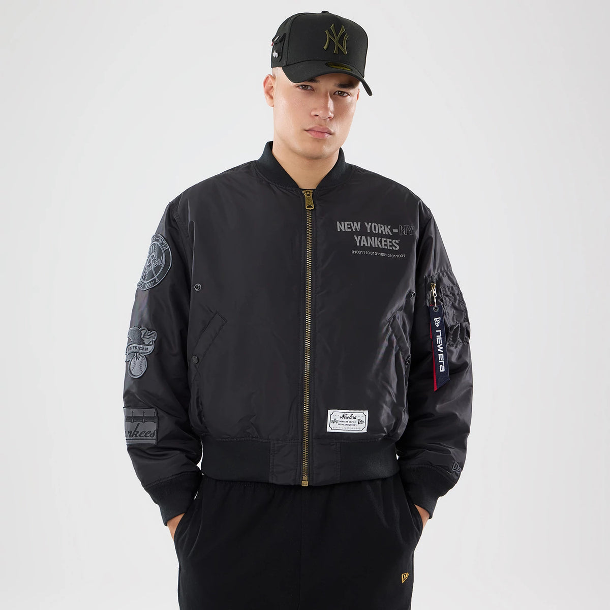 New Era New York Yankees MLB X Alpha Black Bomber Jacket & Tactical Vest, front view on-model showing New York lettering on the right chest, a side zip pocket with a logo tag, and embroidered patches on the sleeves over the dark bomber jacket.