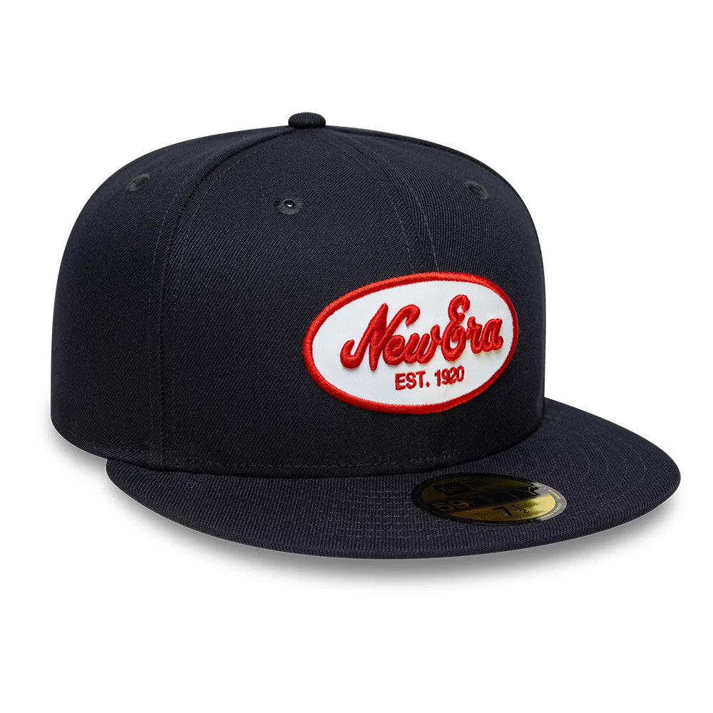 New Era Oval Patch Navy 59FIFTY Fitted Cap, front view showing a red embroidered New Era logo on a white oval patch on the structured navy crown, with a flat visor and a gold 59FIFTY size sticker on the top.