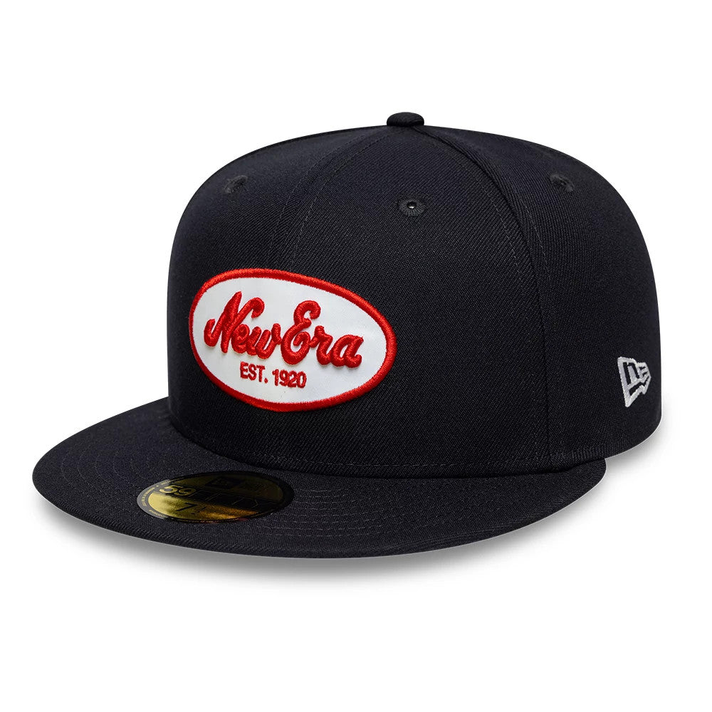 New Era Oval Patch Navy 59FIFTY Fitted Cap, three-quarter view showing the red embroidered New Era oval logo on the front panel, navy flat visor with the gold 59FIFTY size sticker, and the New Era flag logo on the left side.